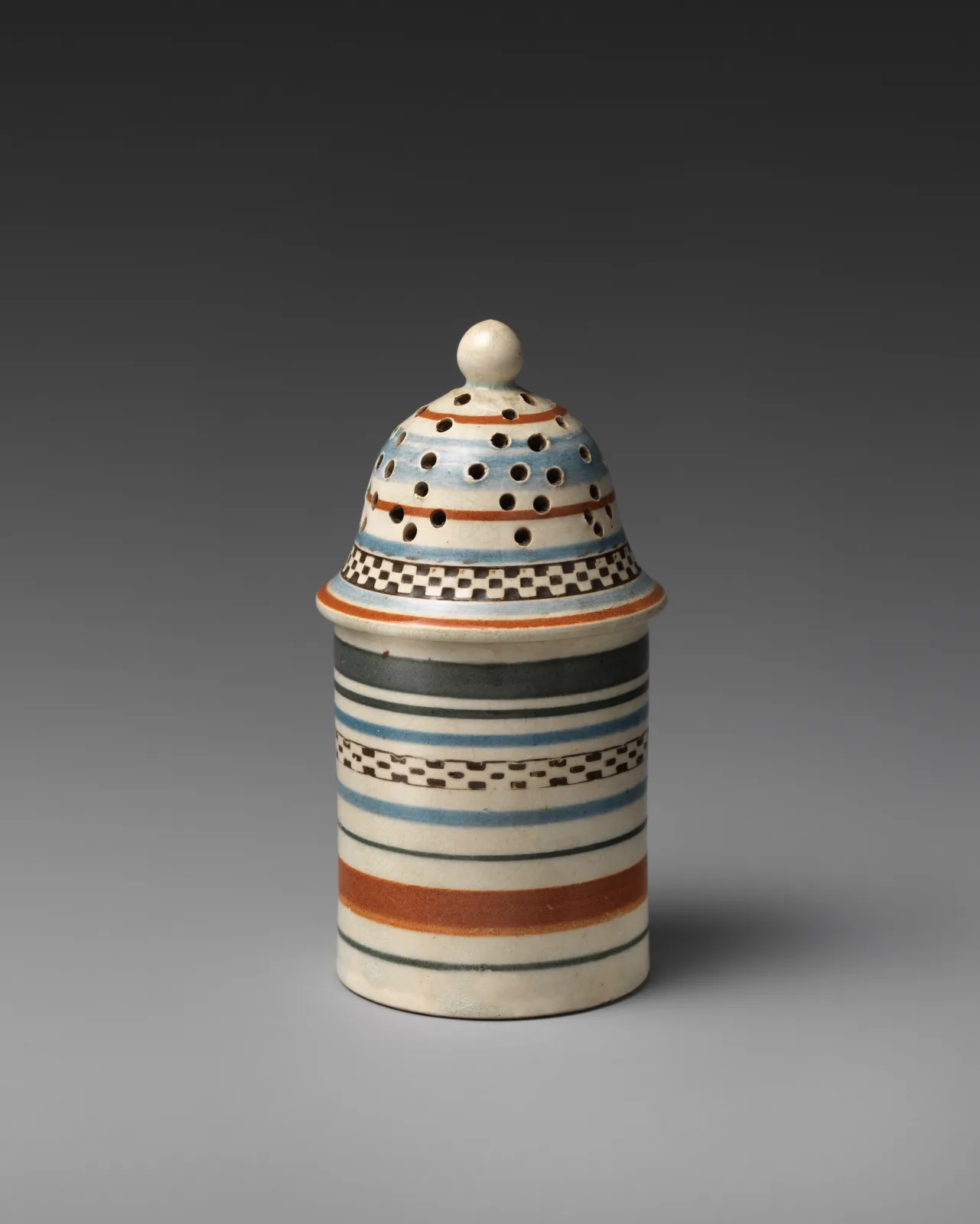 Small cylindrical pepper pot with a domed pierced top, banded in narrow stripes of orange, blue, brown and white, with a row of dark dots around the shoulder