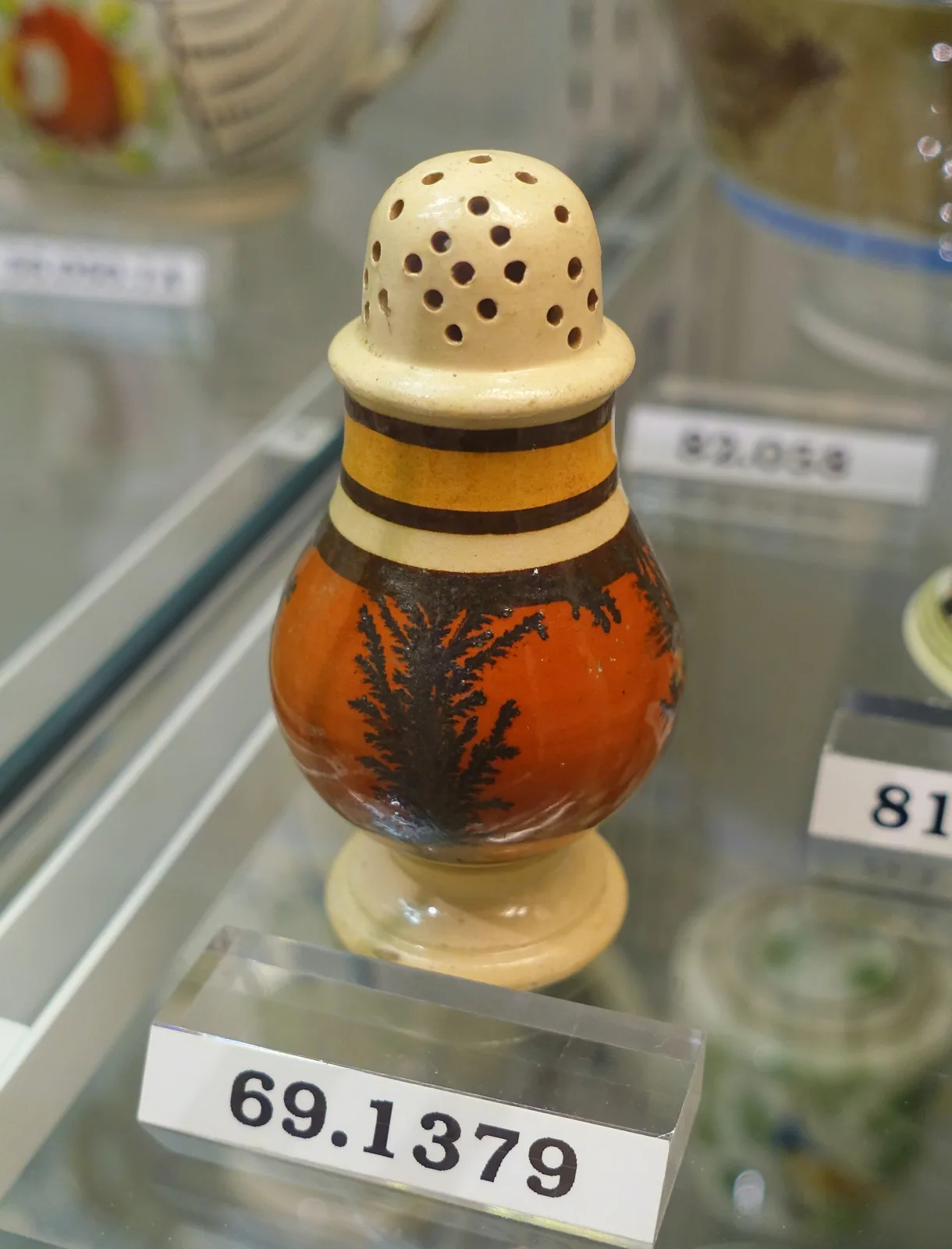 Baluster-shaped caster with a domed pierced top, an orange-brown ground band carrying dark branching dendritic forms, framed by narrow black and cream bands