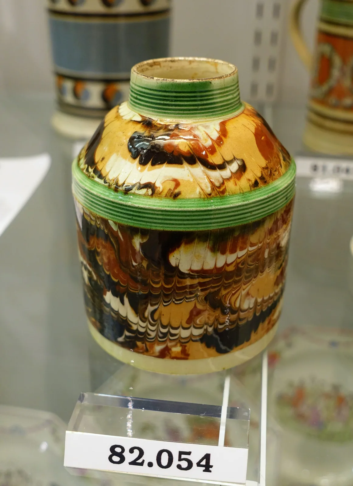 Small cylindrical tea canister with a domed cover, decorated with a broad orange-brown band carrying a looping trailed pattern between narrow green rouletted bands
