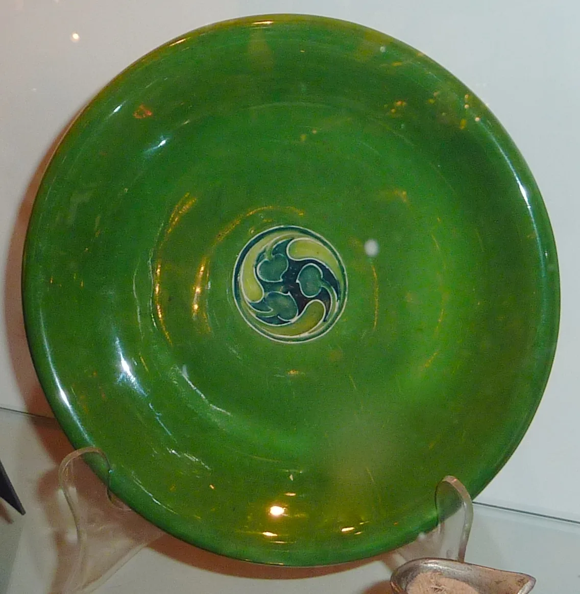 Shallow green dish on a stand, its lustrous monochrome glaze broken only by a small roundel of stylised leaves at the centre