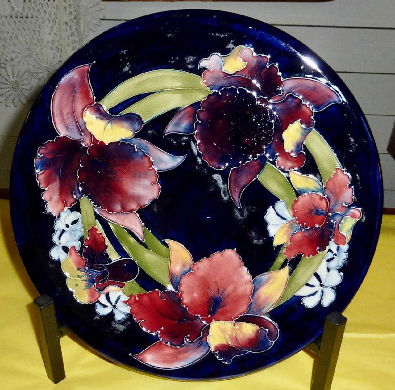 Large circular dish on a stand, its deep cobalt ground filled with crimson and plum irises, green blade leaves and small white flowers, every shape outlined by a raised pale ridge