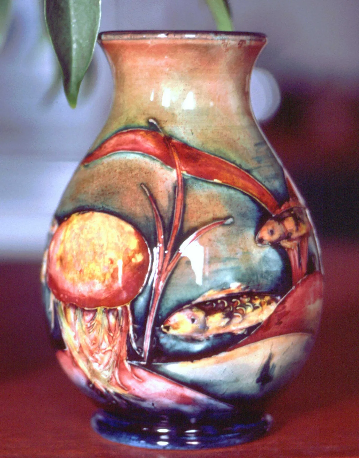 Ovoid vase glazed in mottled orange, red and green, decorated with fish, waterweed and a large round form, each motif outlined in a dark raised line