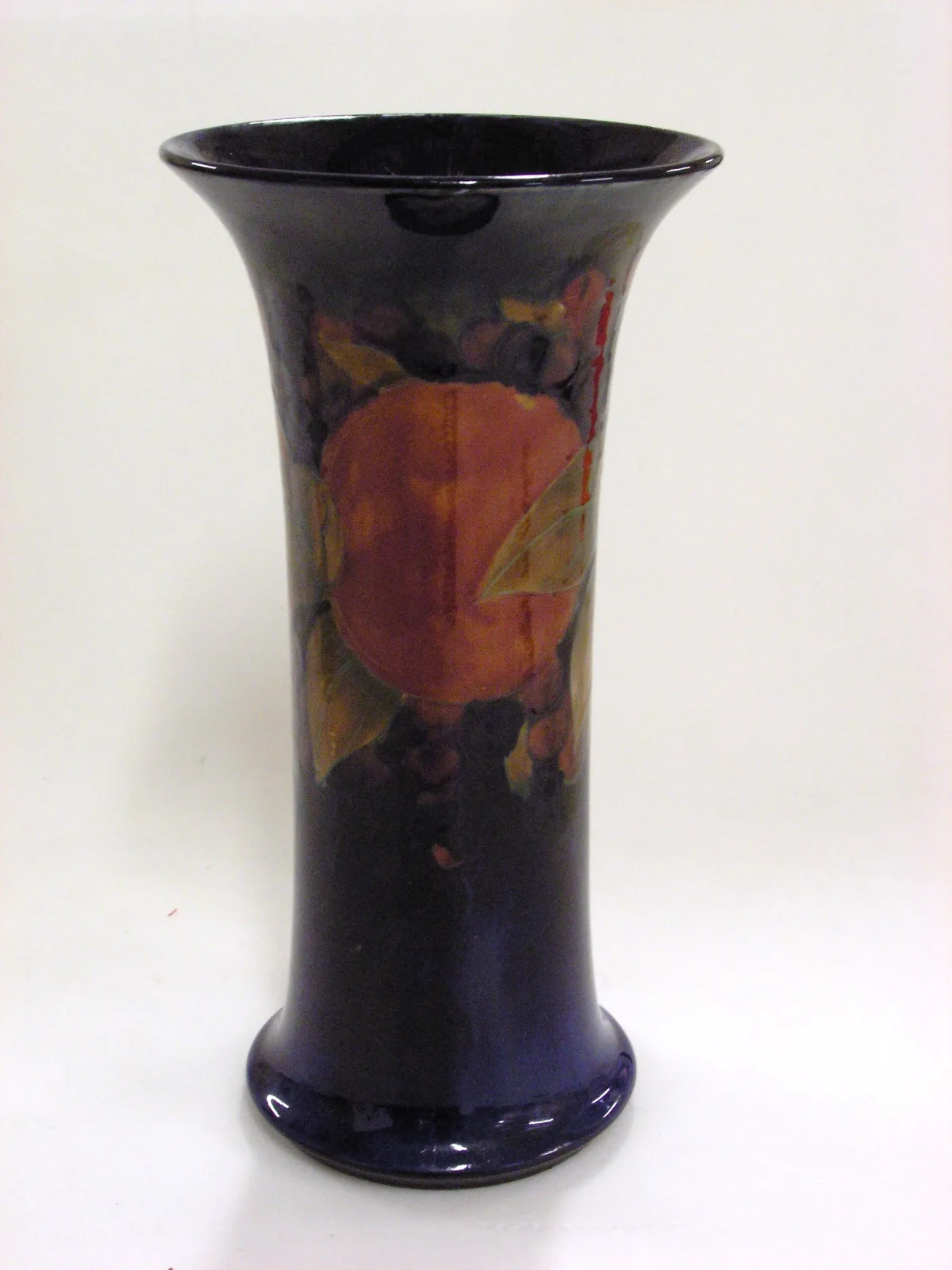 Tall trumpet-shaped vase on a dark blue ground, decorated with a large split pomegranate showing its seeds, with berries and pale green leaves around it