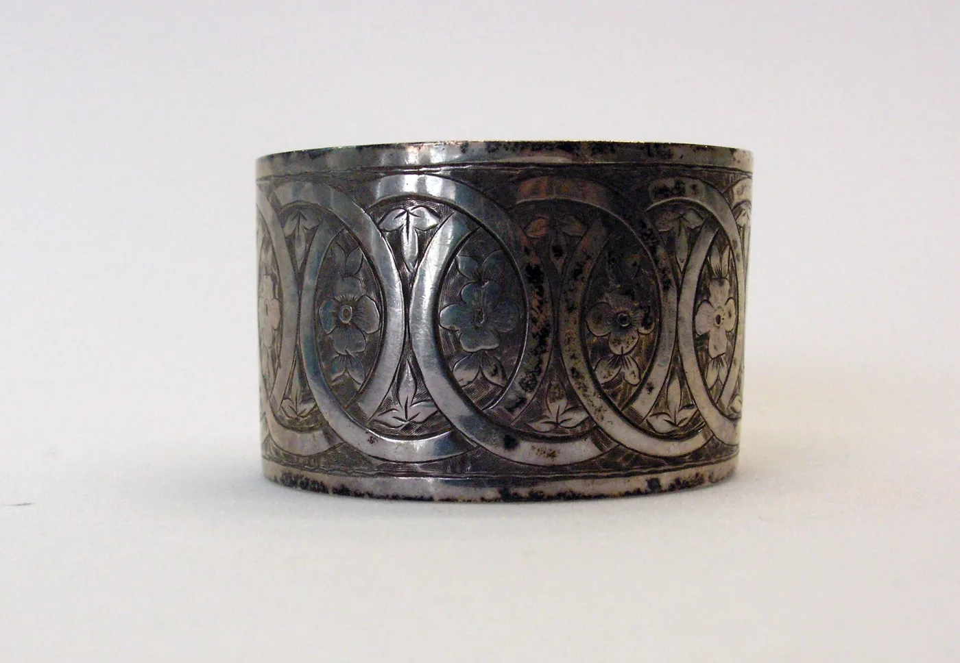 Sterling silver band napkin ring with turned lip edges, engraved with a row of linked ovals each enclosing a four-petalled flower