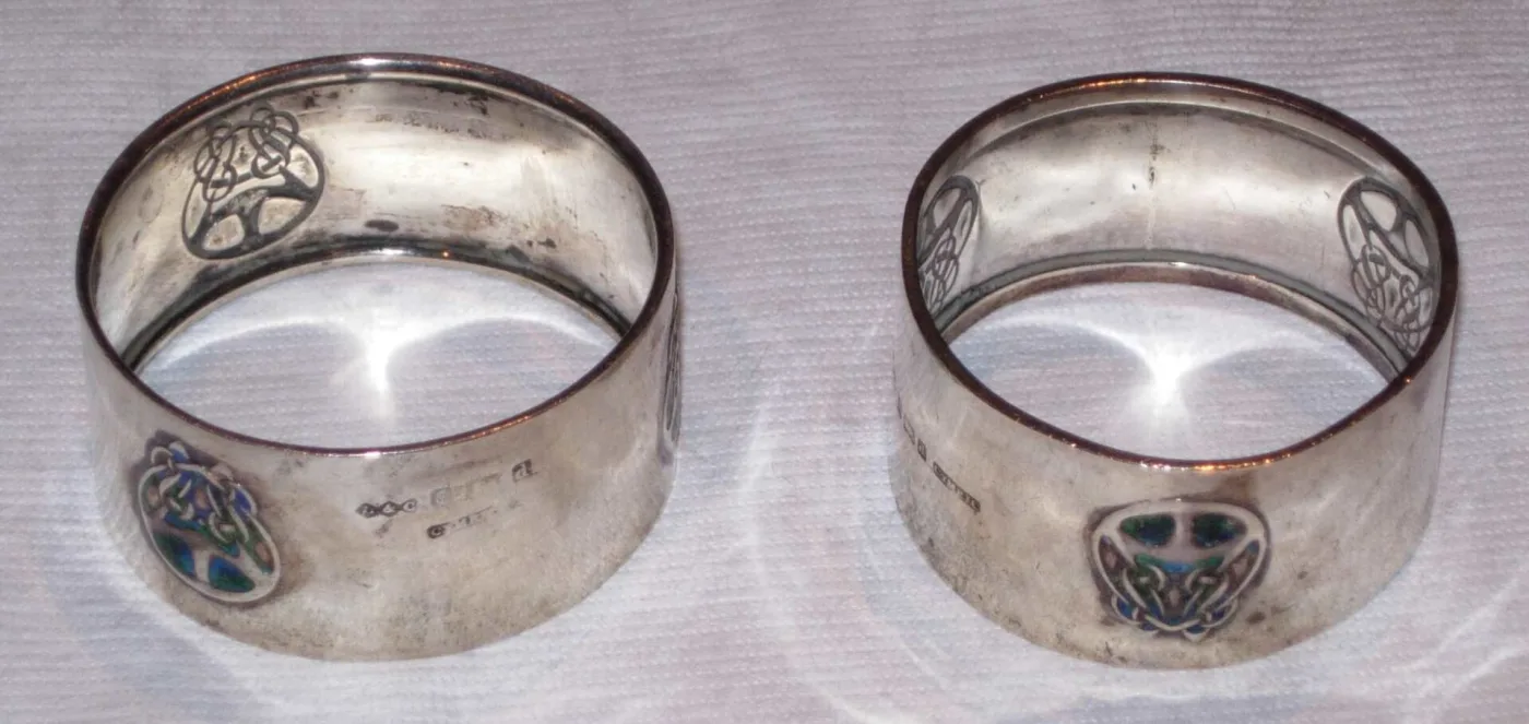 Pair of wide plain silver napkin rings, each with a small blue and green enamelled roundel of entwined Art Nouveau line-work
