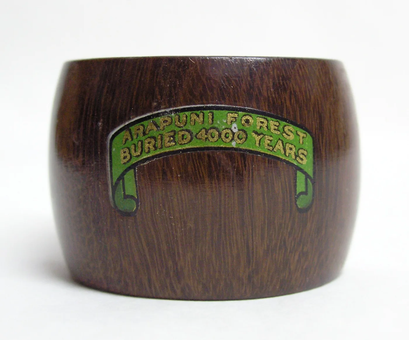 Dark brown turned wooden napkin ring with a green and gold scroll label reading Arapuni Forest buried 4000 years