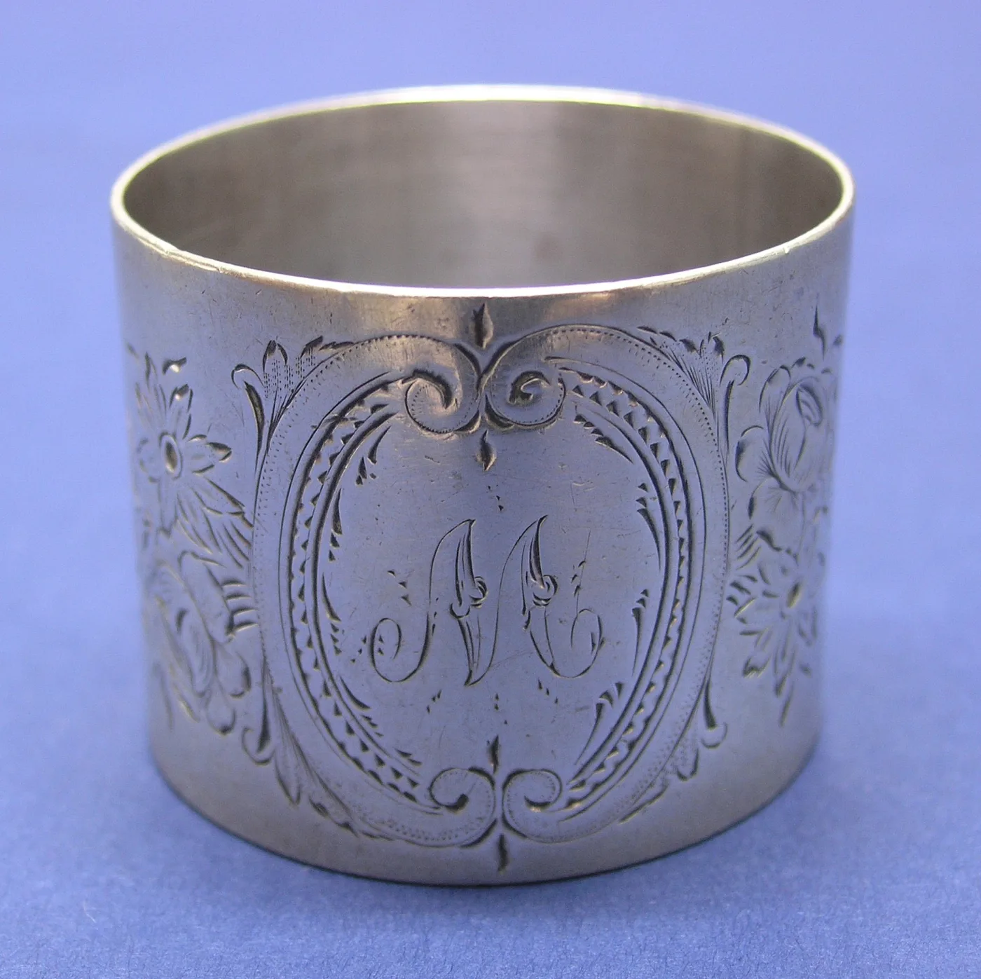 Silver napkin ring engraved with a script M inside a scrolled oval cartouche, with engraved flowers to either side