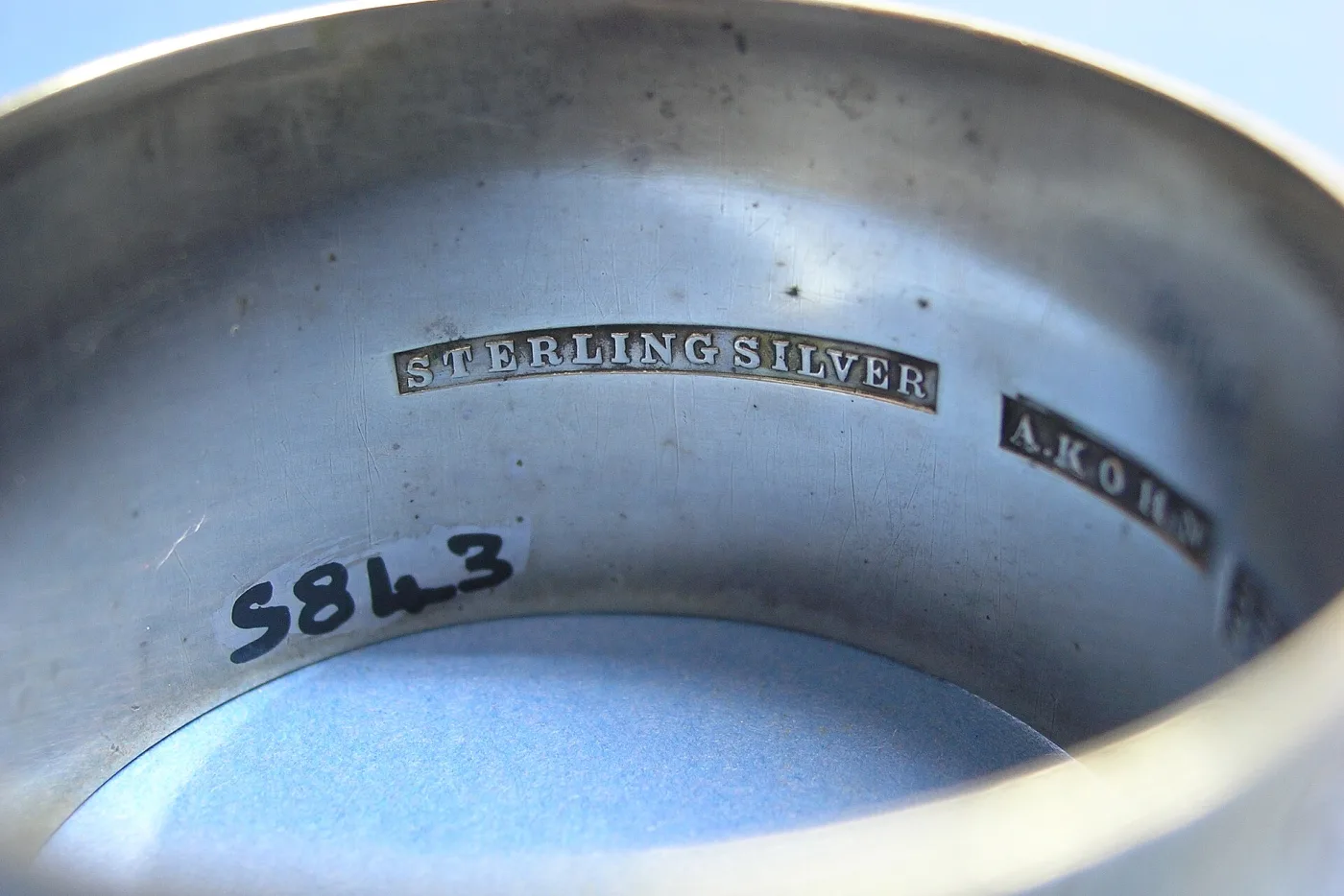 Inside of a silver napkin ring struck with the words STERLING SILVER and a maker's name, with a small inked number below