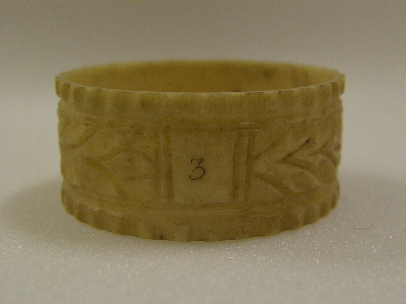 Cream-coloured carved ivory napkin ring with gadrooned rims and foliage, a small numeral 3 written in a plain central panel