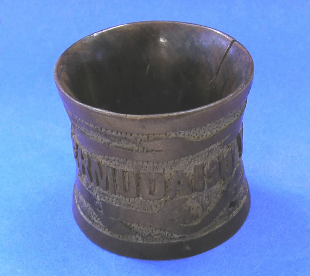 Dark carved wooden napkin ring with a chip-carved banner reading BERMUDA and a date, the rim split by an old crack