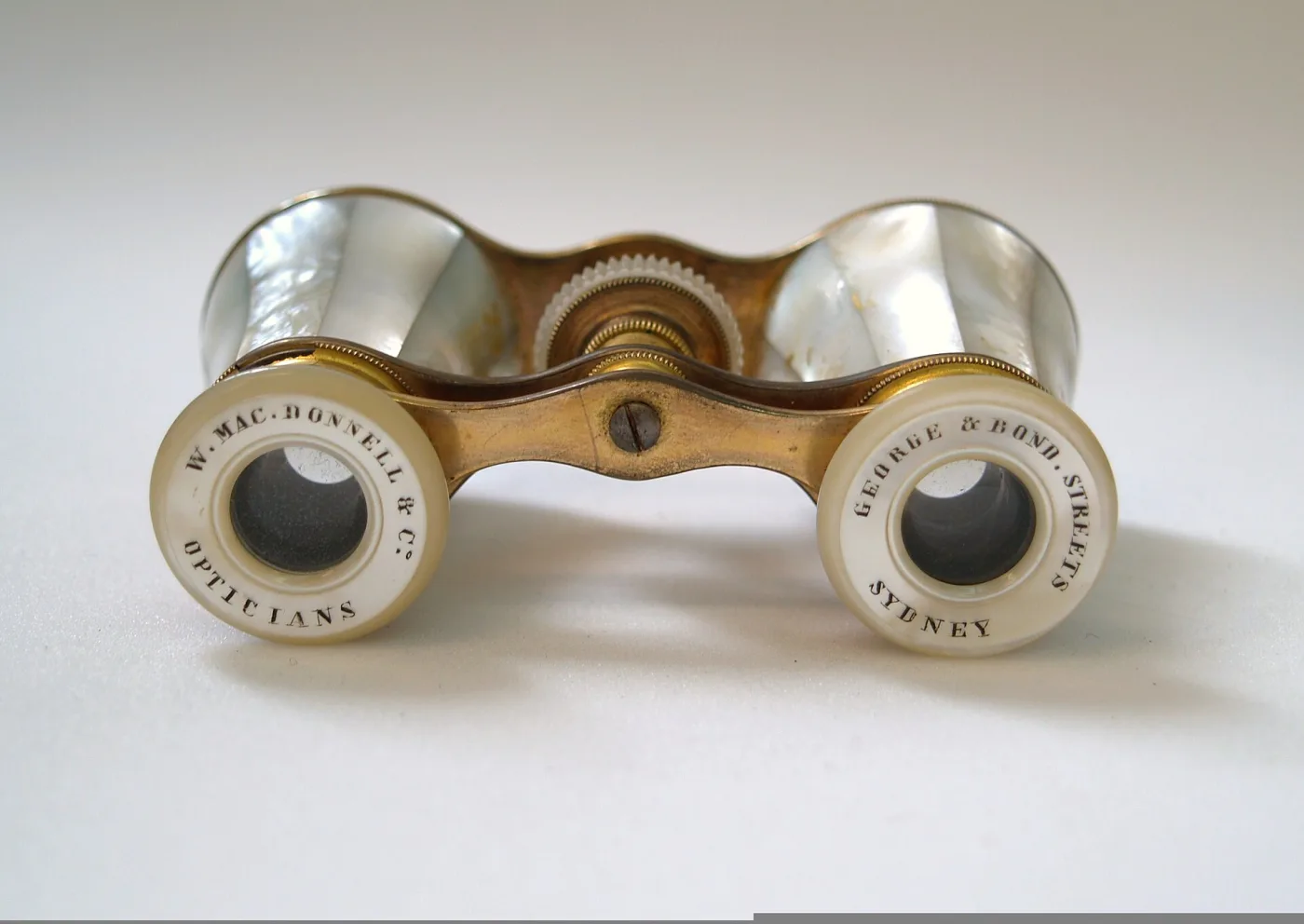 Mother-of-pearl opera glasses seen from the eyepiece end, the two pearl collars lettered W. MacDonnell & Co Opticians and George & Bond Streets Sydney