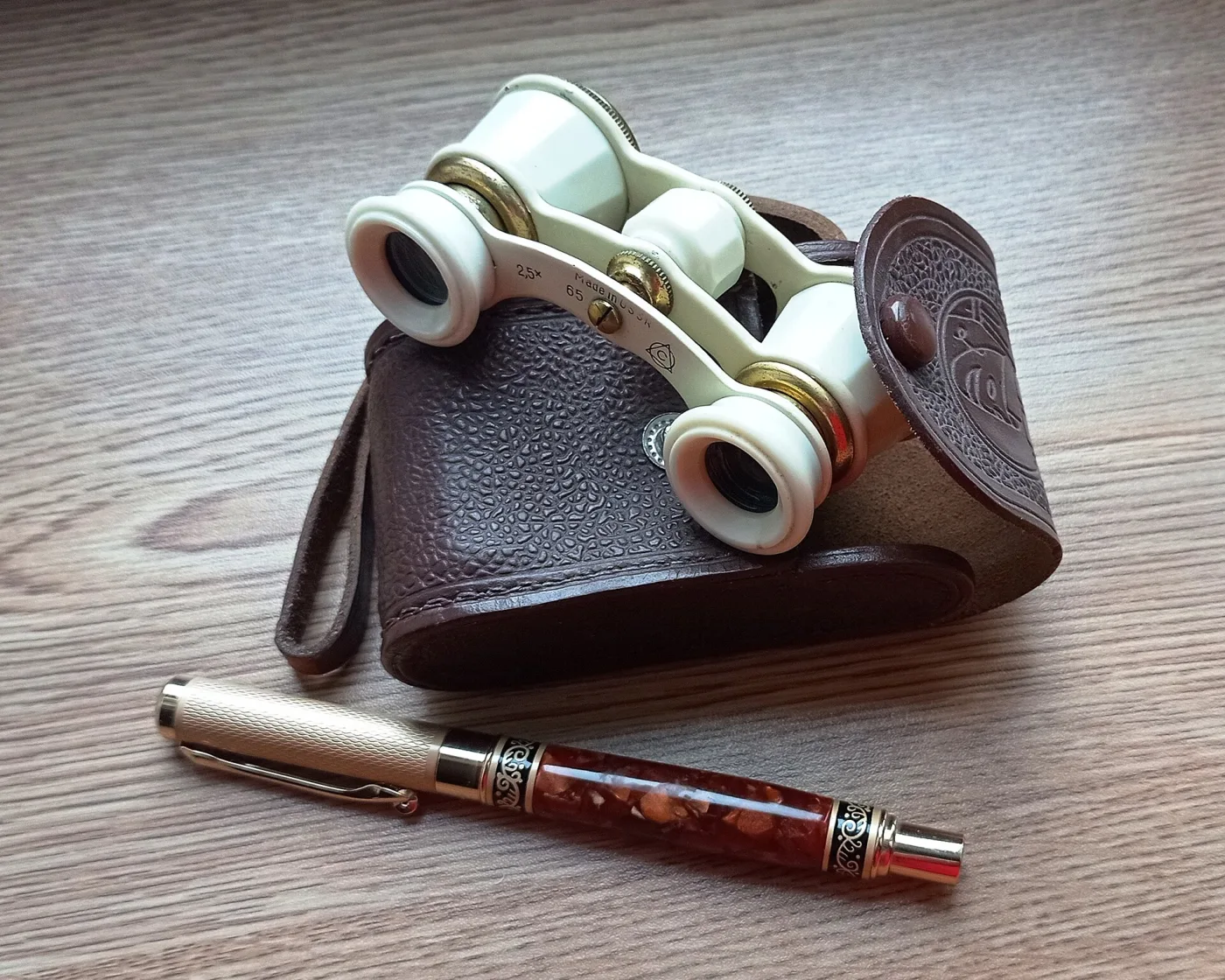 White plastic opera glasses marked 2.5x 65 Made in USSR, resting on a tooled brown leather case
