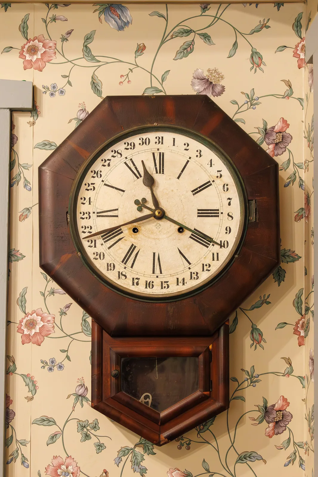 Octagonal wooden wall clock with a painted dial, Roman hour numerals inside an outer ring numbered 1 to 31, and a long calendar hand pointing to 21