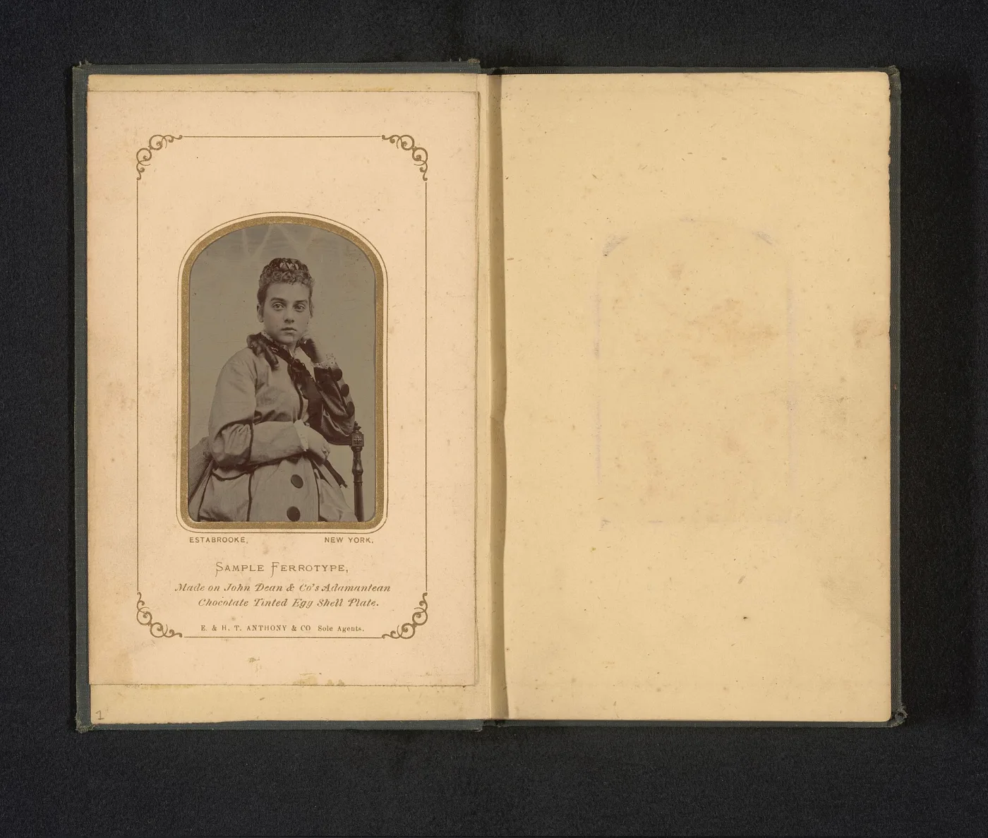 Small oval tintype portrait of a woman mounted in a printed paper folder, the folder opened flat so the blank facing leaf and printed lower margin are visible