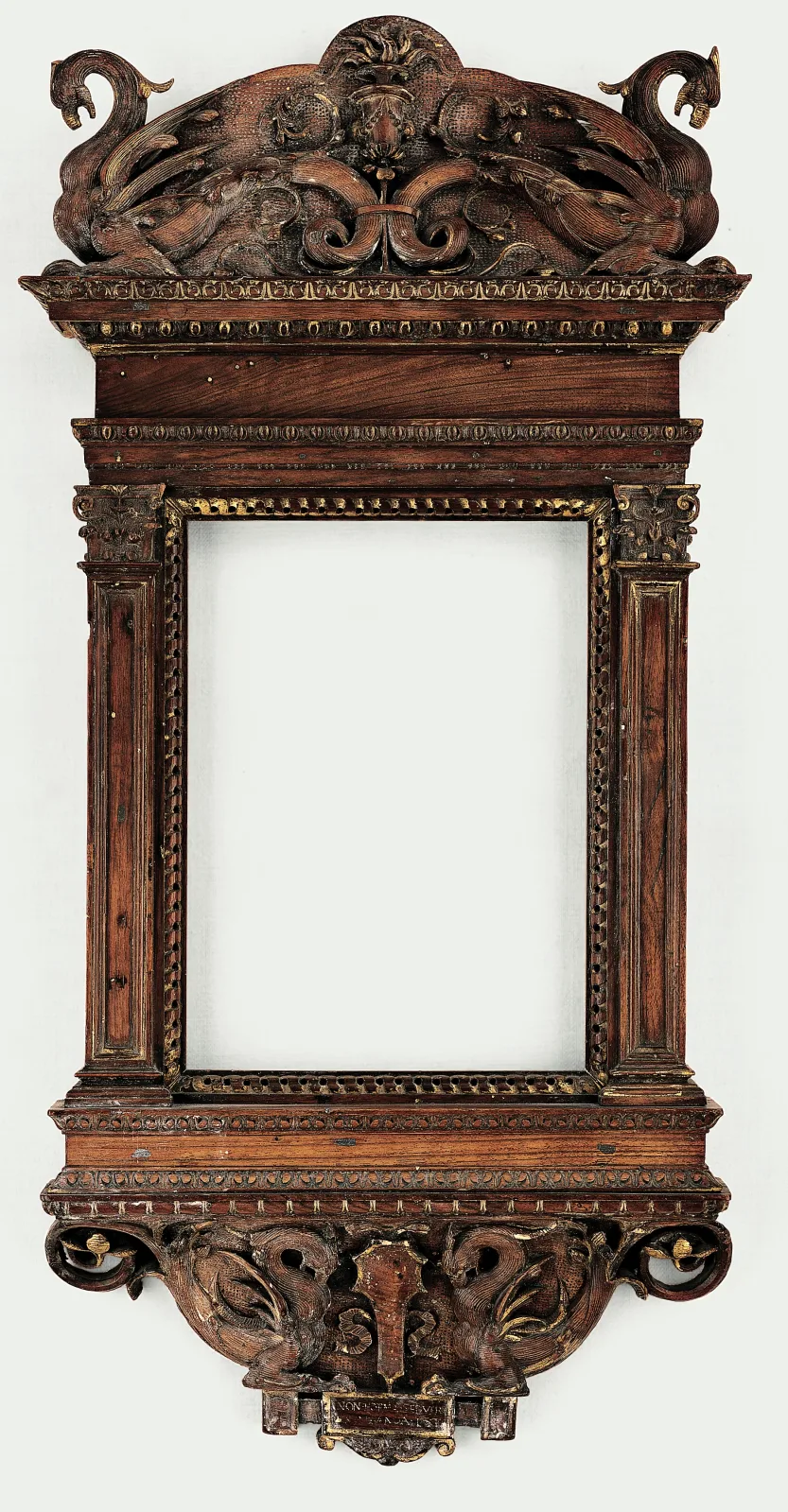 Carved walnut tabernacle frame of about 1530 with an ungilded brown surface, a crest of grotesque dolphins and foliage, fluted pilasters, and a scrolled console shelf beneath the aperture