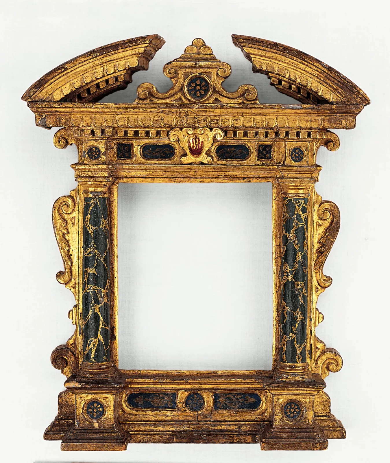 Early seventeenth-century Italian tabernacle picture frame in carved and gilded wood, with a broken segmental pediment, flanking columns, dark inlaid panels in the frieze and base, and scrolled side wings