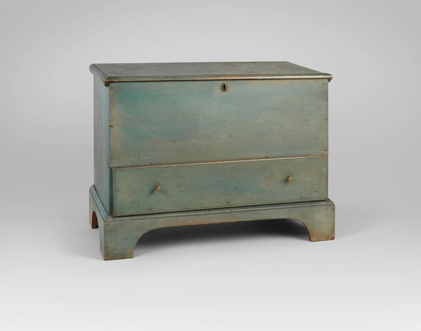 Shaker blanket chest painted blue-green, closed, with a plain lid, a single long drawer at the bottom and a cut-out bracket base, photographed against a grey ground