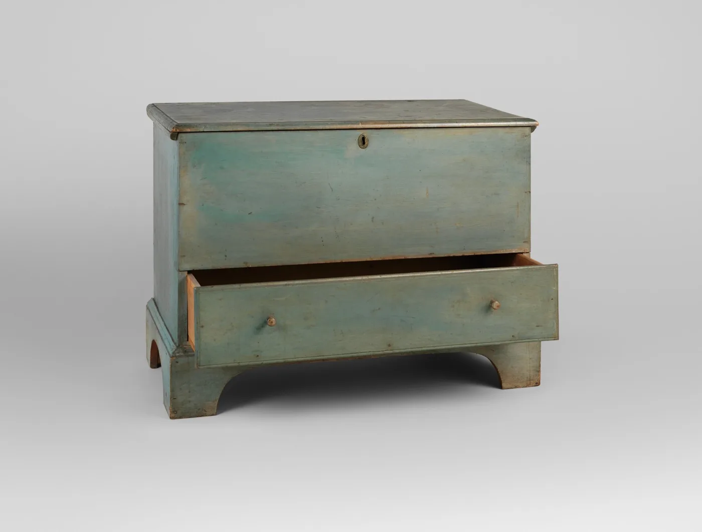 The same chest with its long bottom drawer pulled open, showing the pale unpainted wood of the drawer side and interior against the blue-green painted front