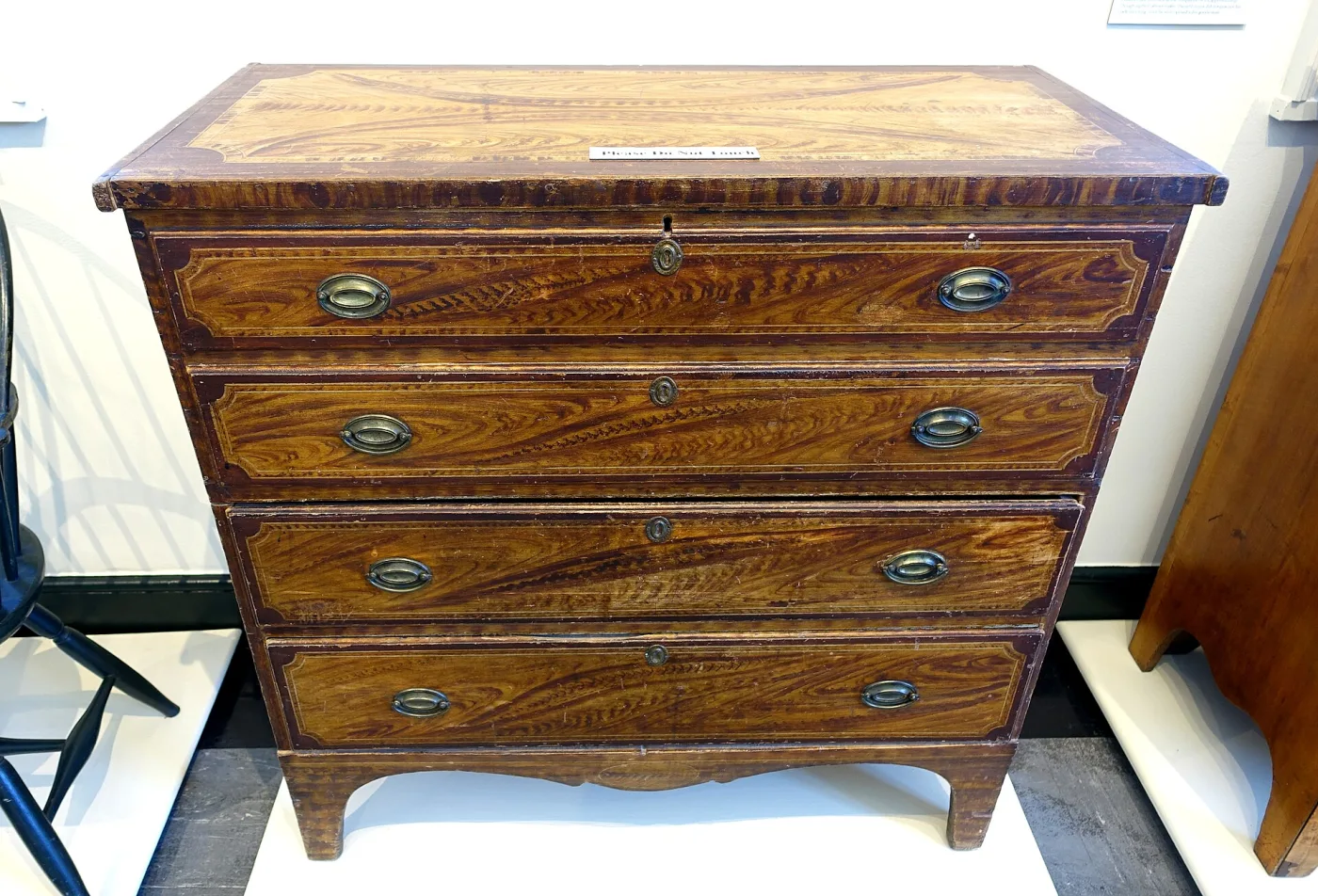 Four-drawer chest of about 1825 whose entire surface is grain-painted in swirling amber and dark brown to imitate figured hardwood, with oval stamped brass pulls and shaped French feet