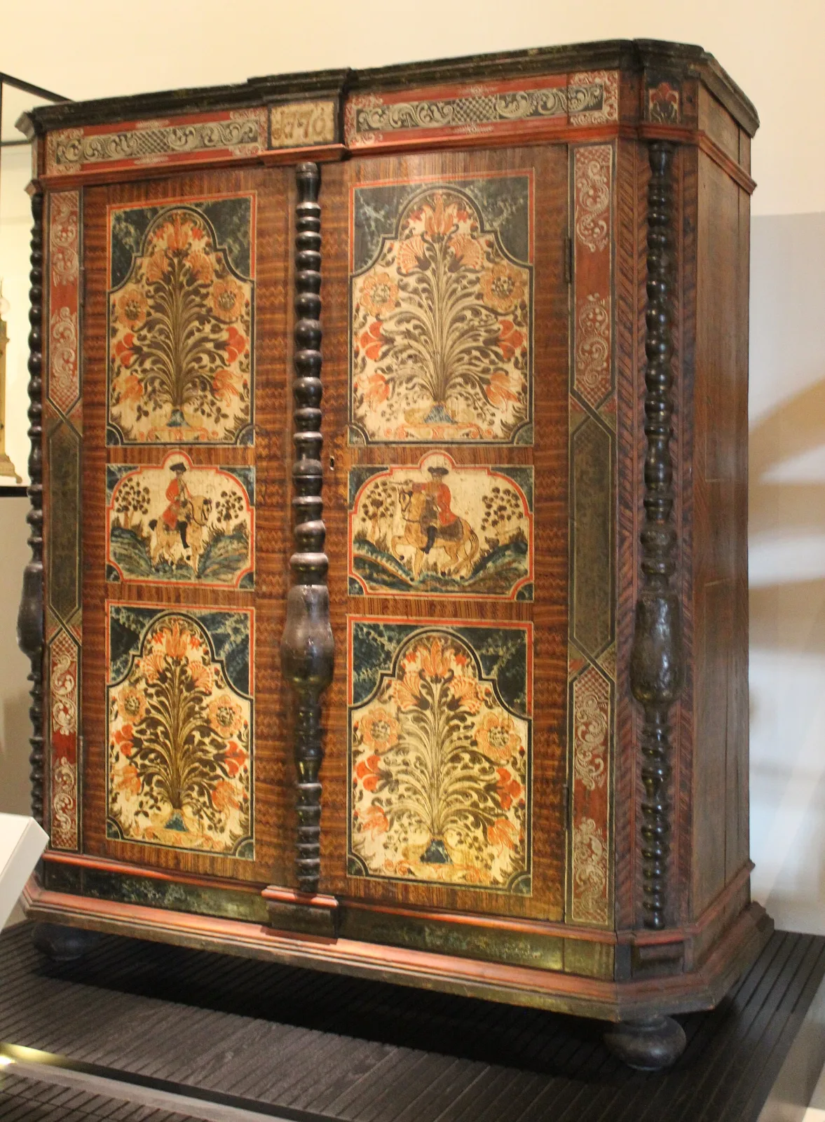 Tall painted pine cupboard from Upper Austria dated 1776, with two doors framed by spiral-turned columns, panels of stylised flowering trees and figures, and combed graining across the surrounding surfaces