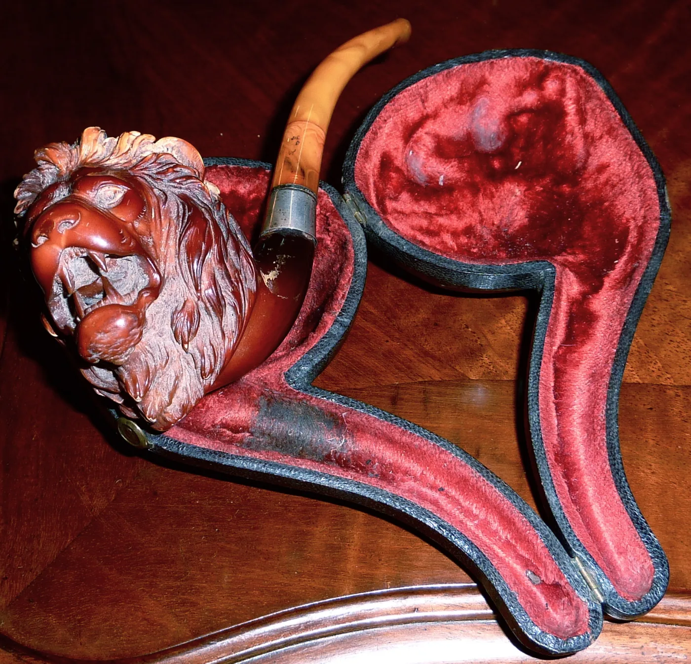 Meerschaum pipe carved as a roaring lion's head, deeply coloured red-brown, lying in its shaped velvet-lined case
