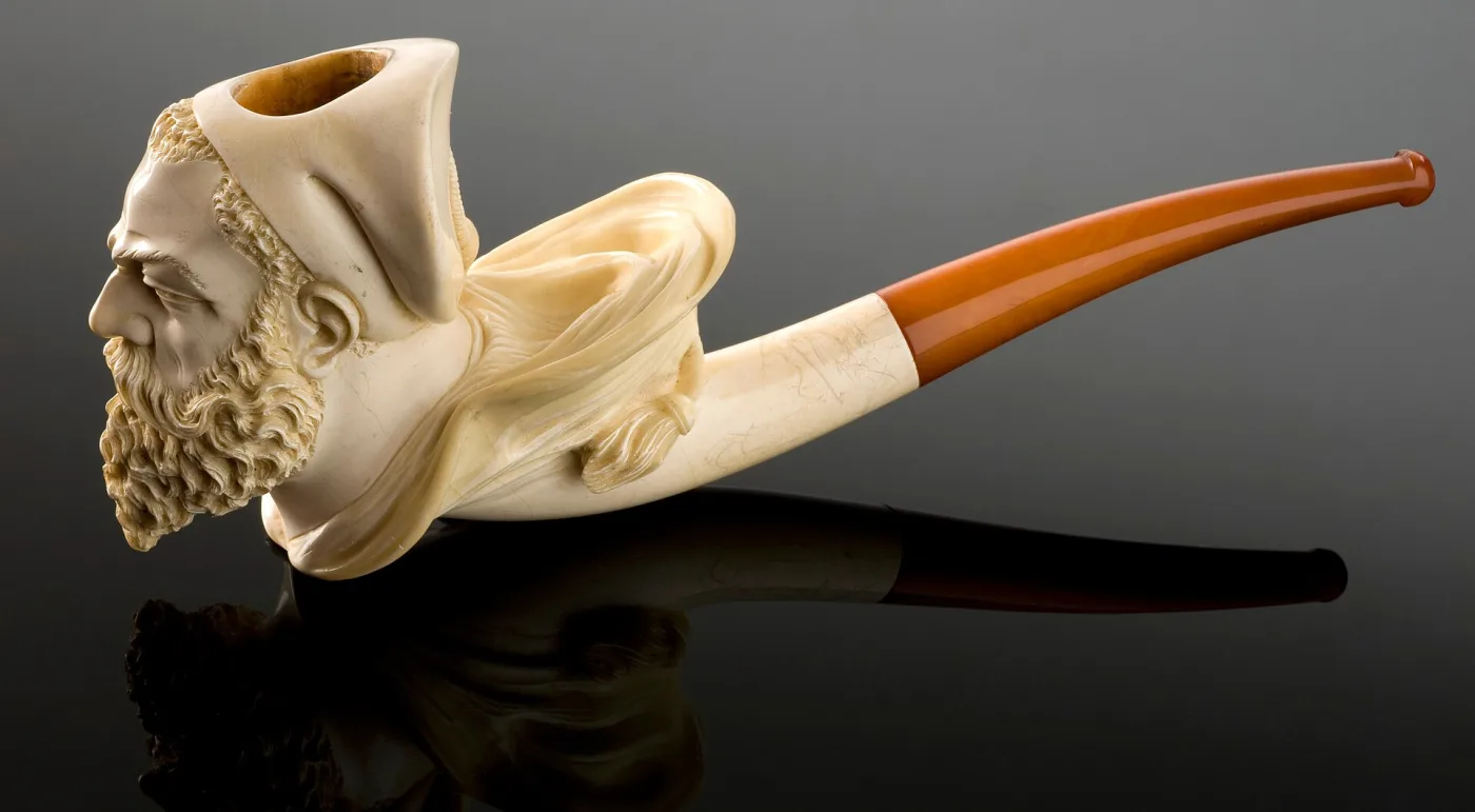 Cream-white meerschaum pipe carved as a bearded man's head, fitted with a long curved amber stem
