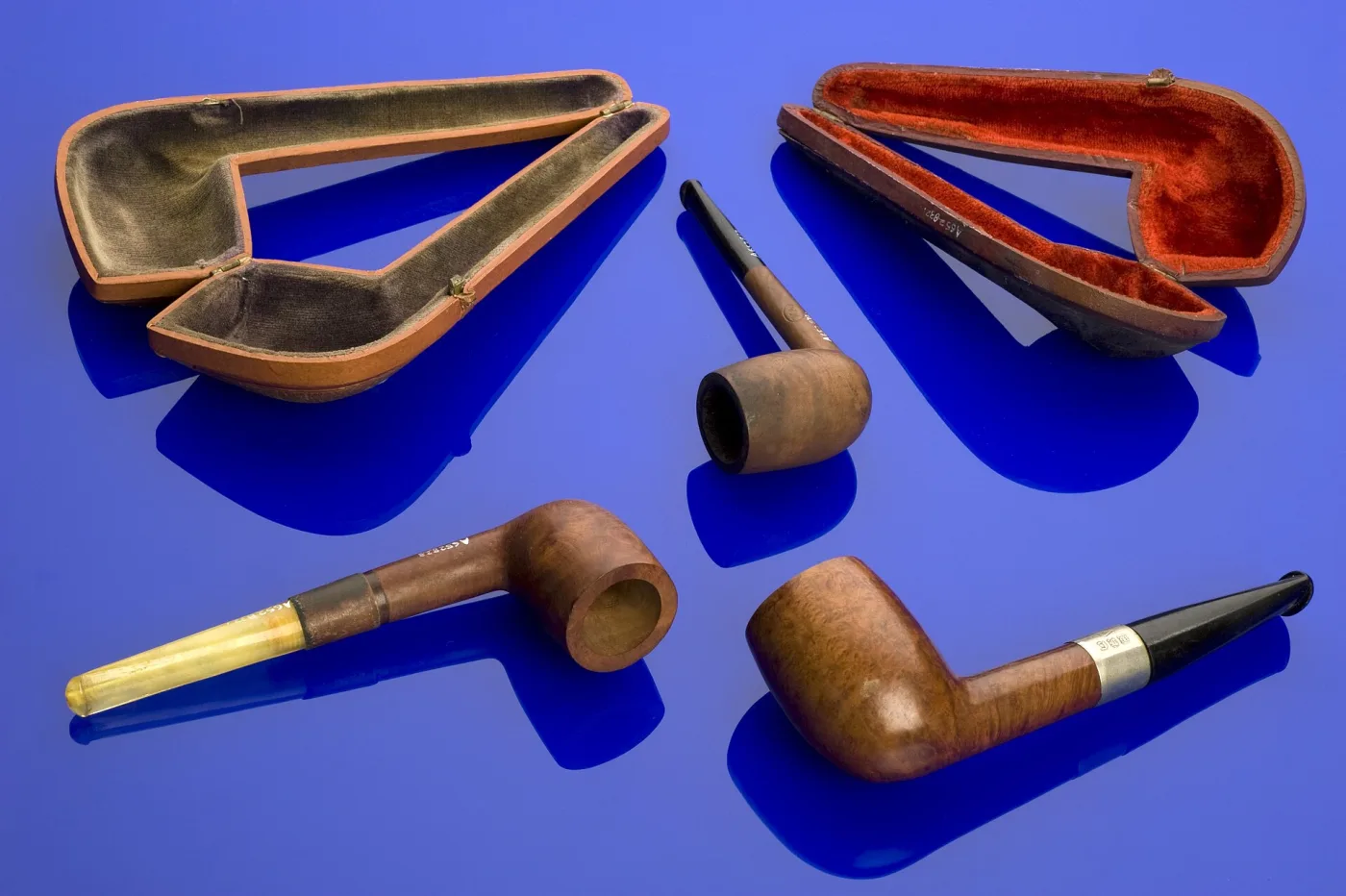 Three briar pipes with their shaped fitted cases, one with a pale amber stem, one with a hallmarked silver band and black stem