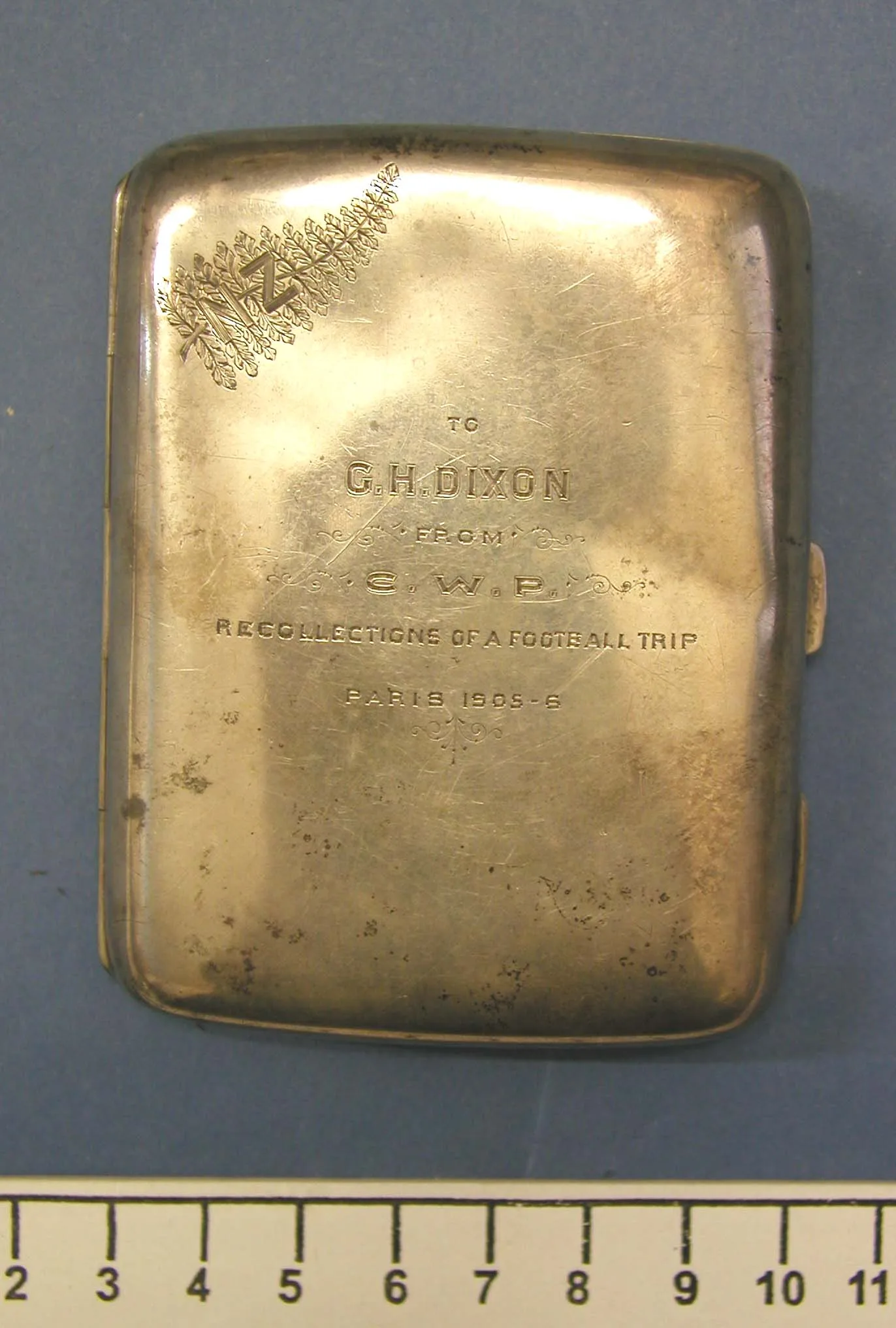 Plain silver cigarette case engraved with a fern-and-monogram badge above a presentation inscription dated Paris 1905-6