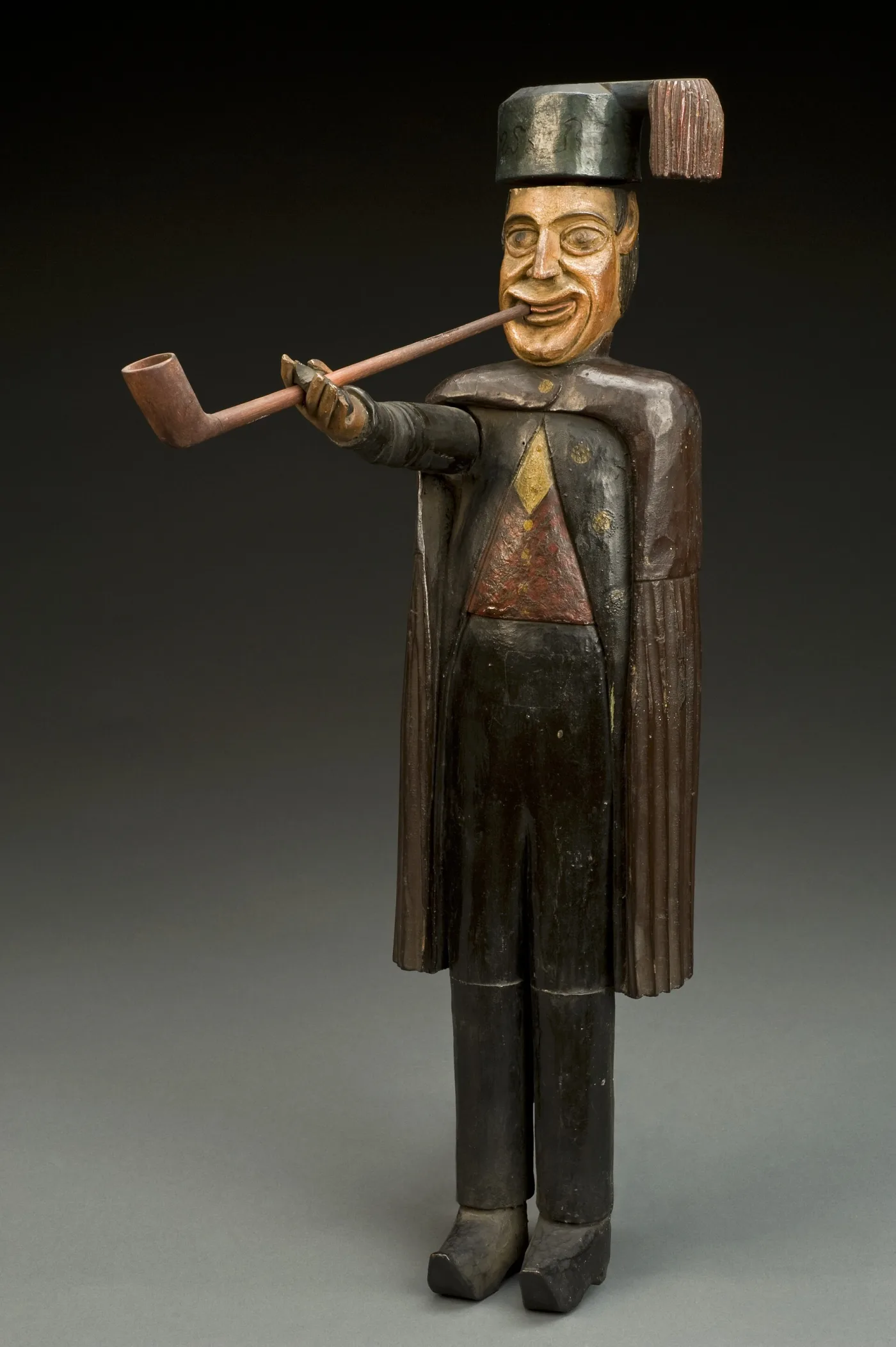 Carved and painted wooden shop figure of a smiling officer in a cape, holding a long-stemmed pipe to his mouth