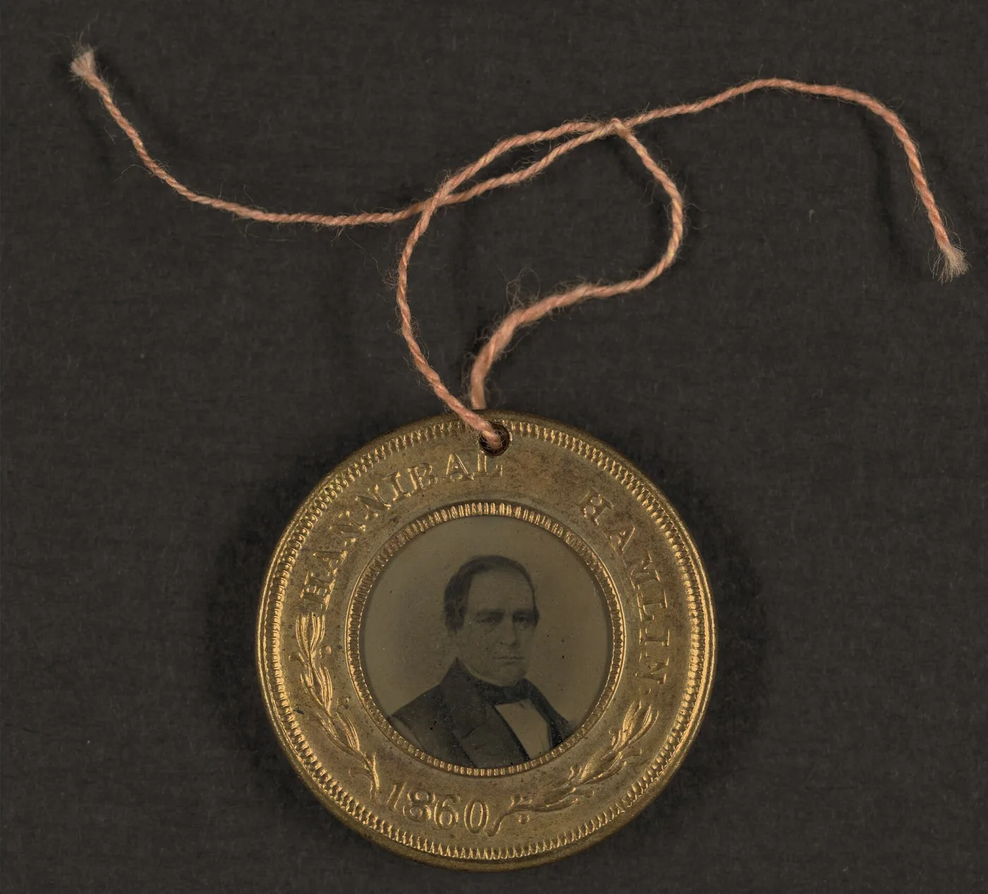 Reverse of the same style of 1860 brass campaign badge, holding a tintype portrait of Hannibal Hamlin in a matching stamped rim, with the original cord still threaded through