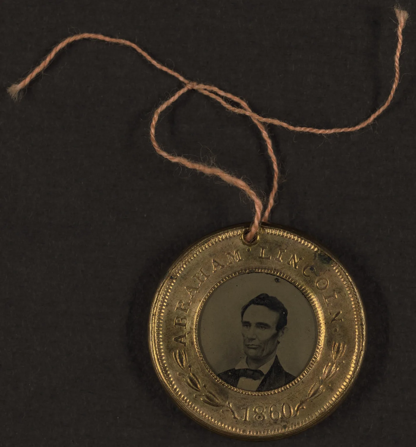 Front of an 1860 brass campaign badge holding a tintype portrait of Abraham Lincoln, beardless, in a stamped rim