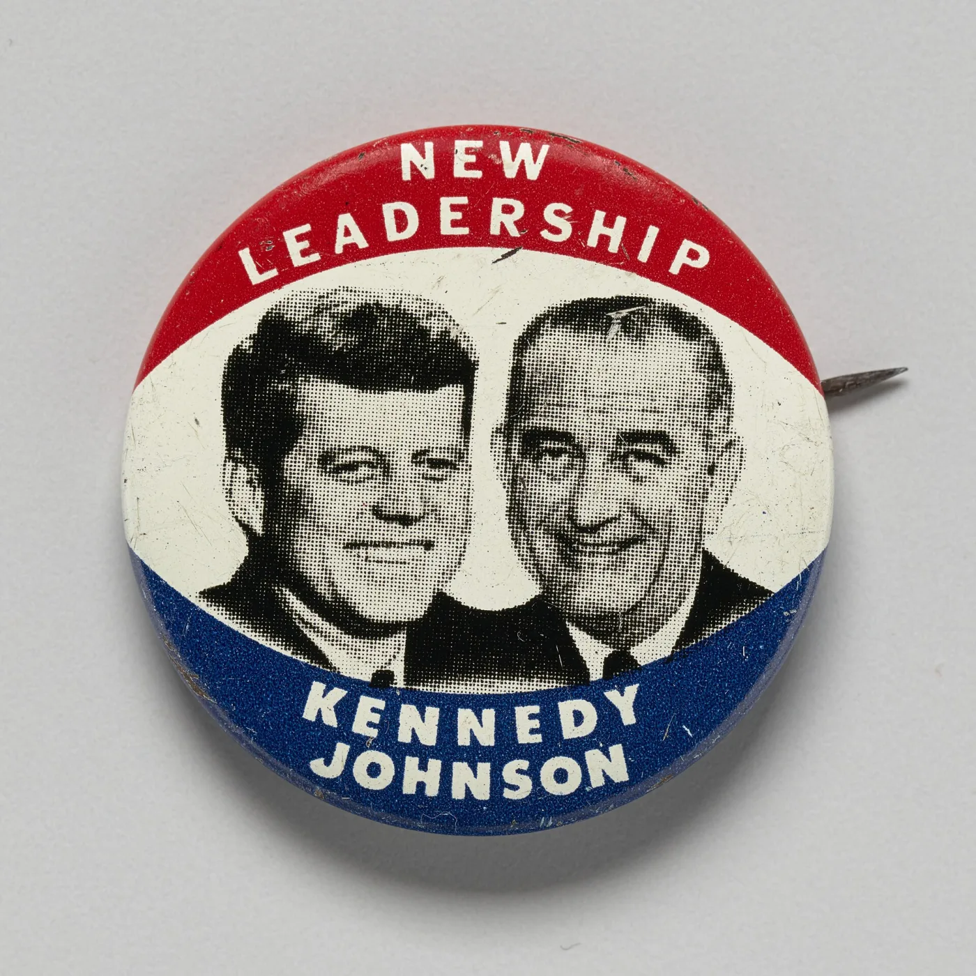 Round 1960 celluloid campaign button with red, white and blue bands, black-and-white photographic portraits of John F. Kennedy and Lyndon Johnson side by side, the words NEW LEADERSHIP above and KENNEDY JOHNSON below