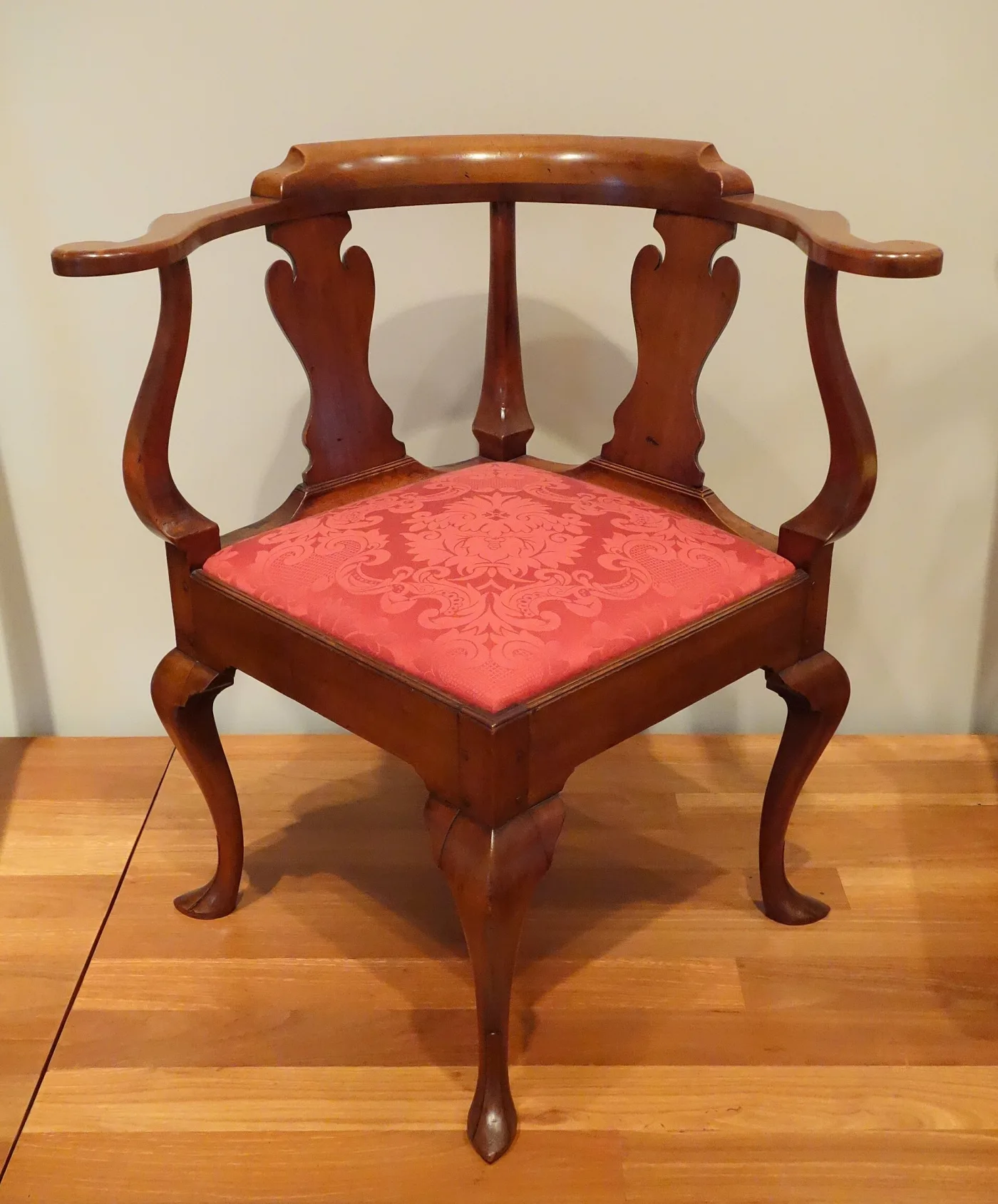 Cherry corner chair with a horseshoe crest rail continuing into scrolled arms, two solid vase splats, a red slip seat and a shaped front cabriole leg