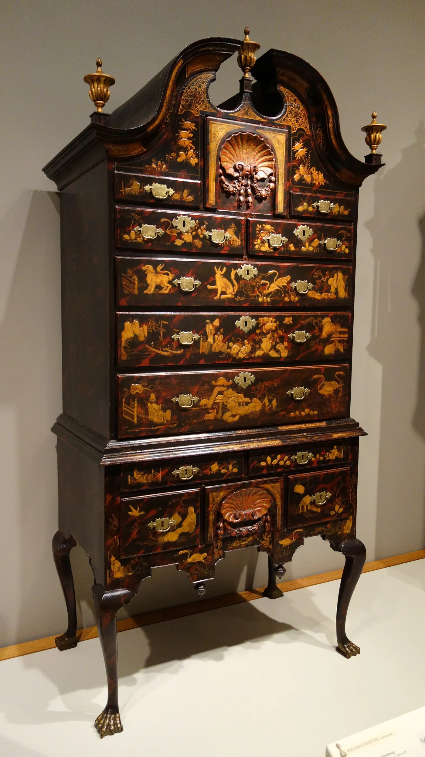 High chest japanned in black and gold with raised chinoiserie figures, animals and landscapes, gilt urn finials and claw-and-ball feet