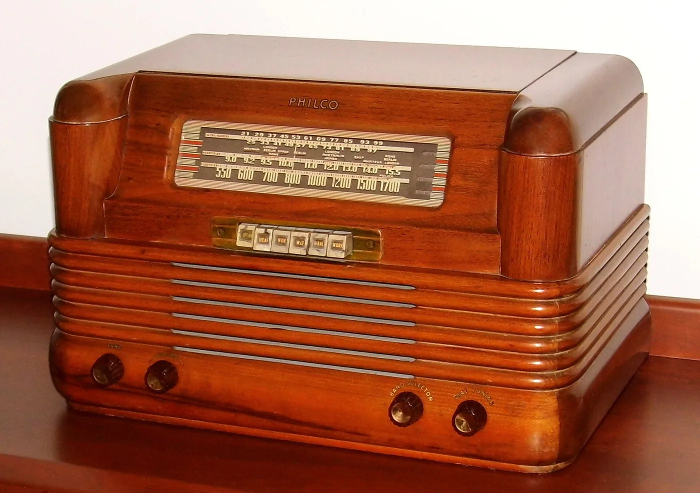 Horizontal wooden table radio with rounded ends, a wide slide-rule dial and a brass strip of six labelled push buttons below it