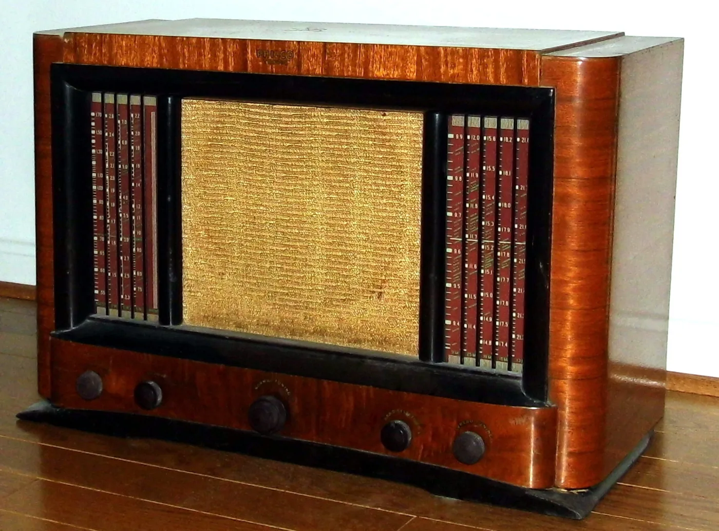 Wide wooden radio with a gold cloth grille flanked by two tall vertical dial scales printed in red and white, above five knobs