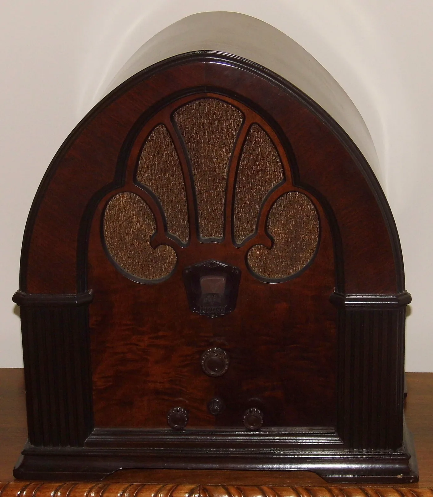 Arched walnut cathedral radio with a fleur-de-lis fretwork grille, a small central dial window and knobs below