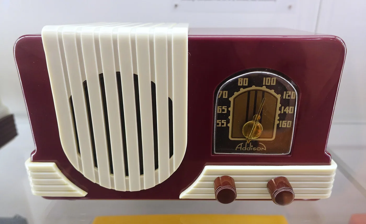 Maroon plastic table radio with a cream ribbed speaker grille, cream knob plinth and an arched gold dial