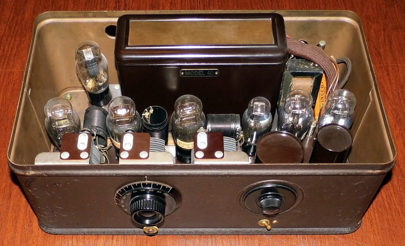 Open metal box radio seen from above, holding seven glass tubes in rows beside a black metal cover plate labelled Model 40