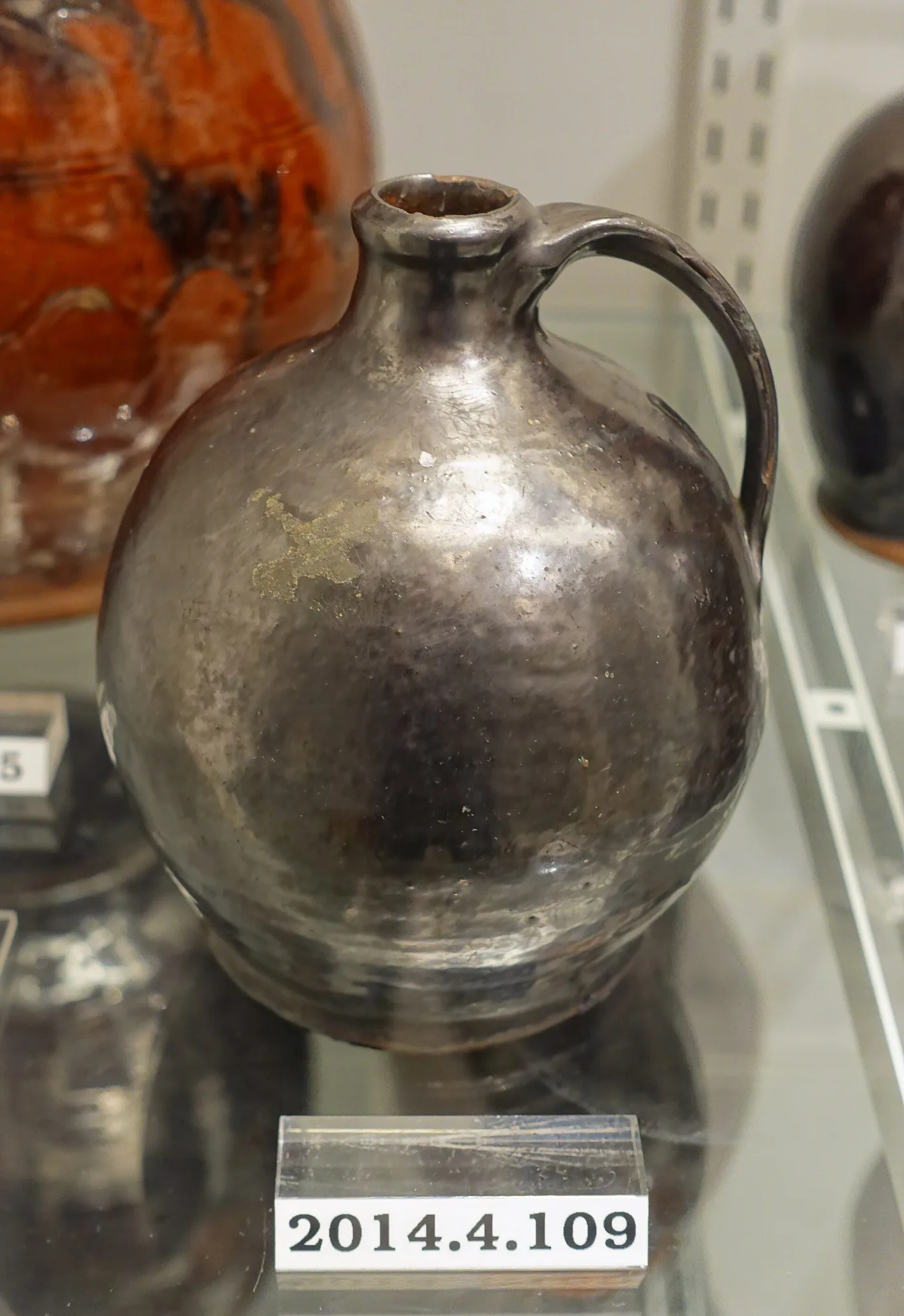 Squat redware jug with a strap handle under a near-black glossy manganese glaze