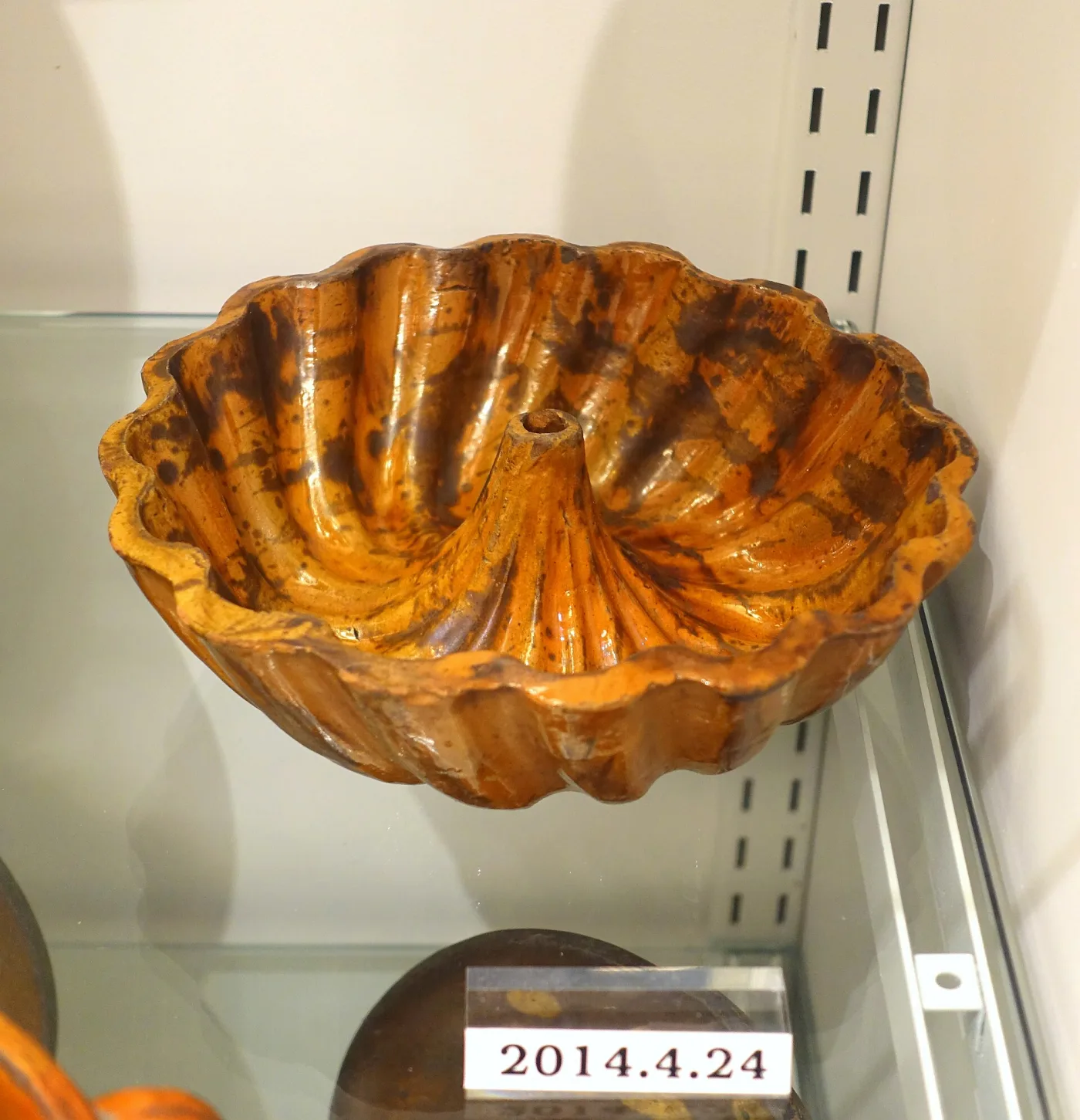 Fluted redware cake mould with a hollow central cone, glazed orange with dark brown mottling