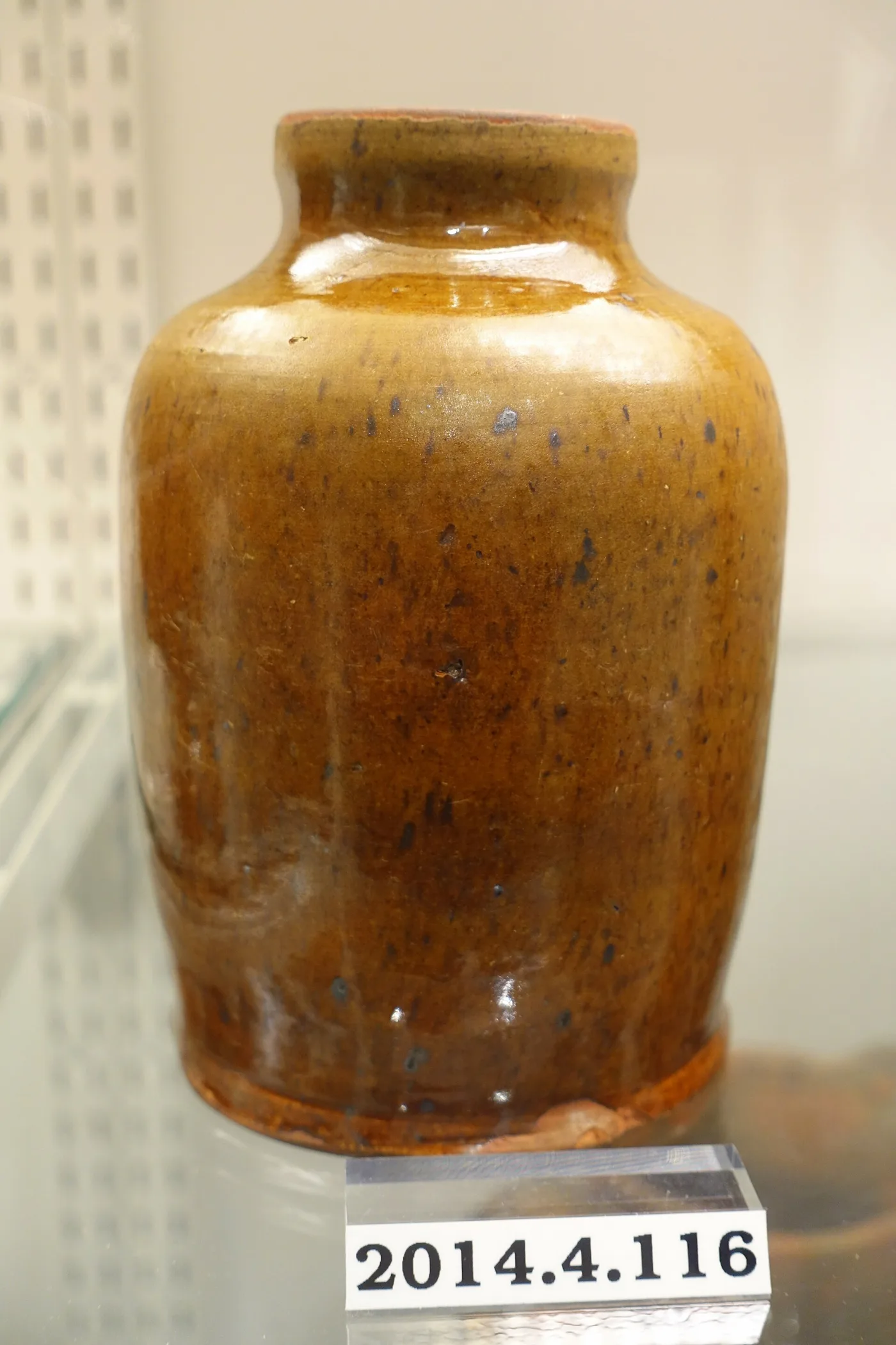Cylindrical redware storage jar with a glossy amber-brown speckled glaze, unglazed at the rim and around the base