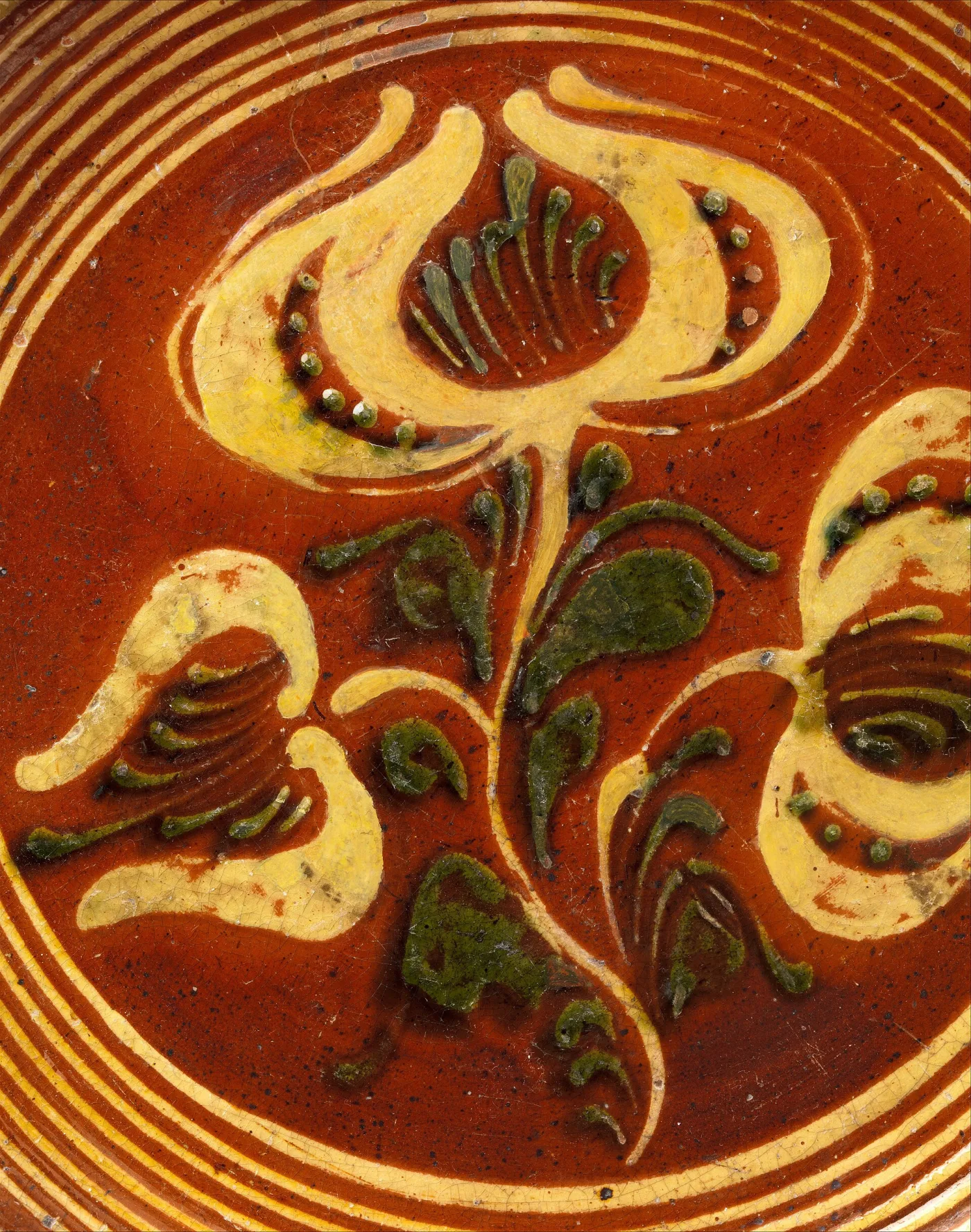 Close view of trailed cream and green slip forming a tulip on a dark red glazed ground, with fine crazing across the whole surface