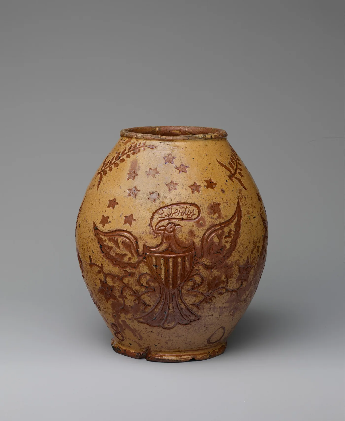 Ovoid cream-slipped redware jar incised with an American eagle holding a shield, ringed by stars, with a date at the base