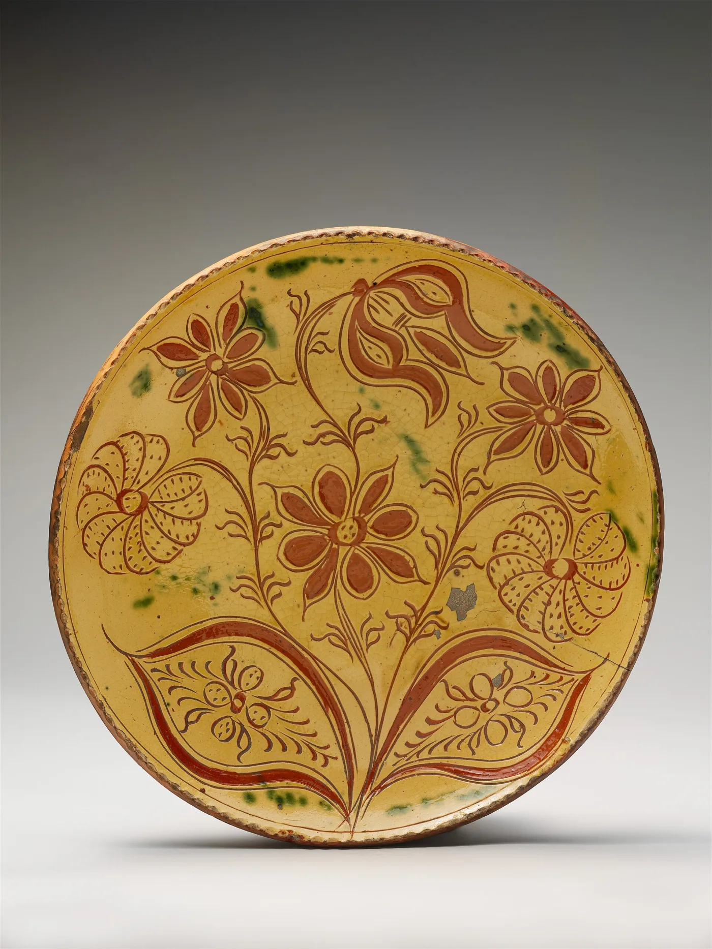 Yellow-slipped plate incised with flowers and tulips, green splashes, and chips at the rim exposing red clay