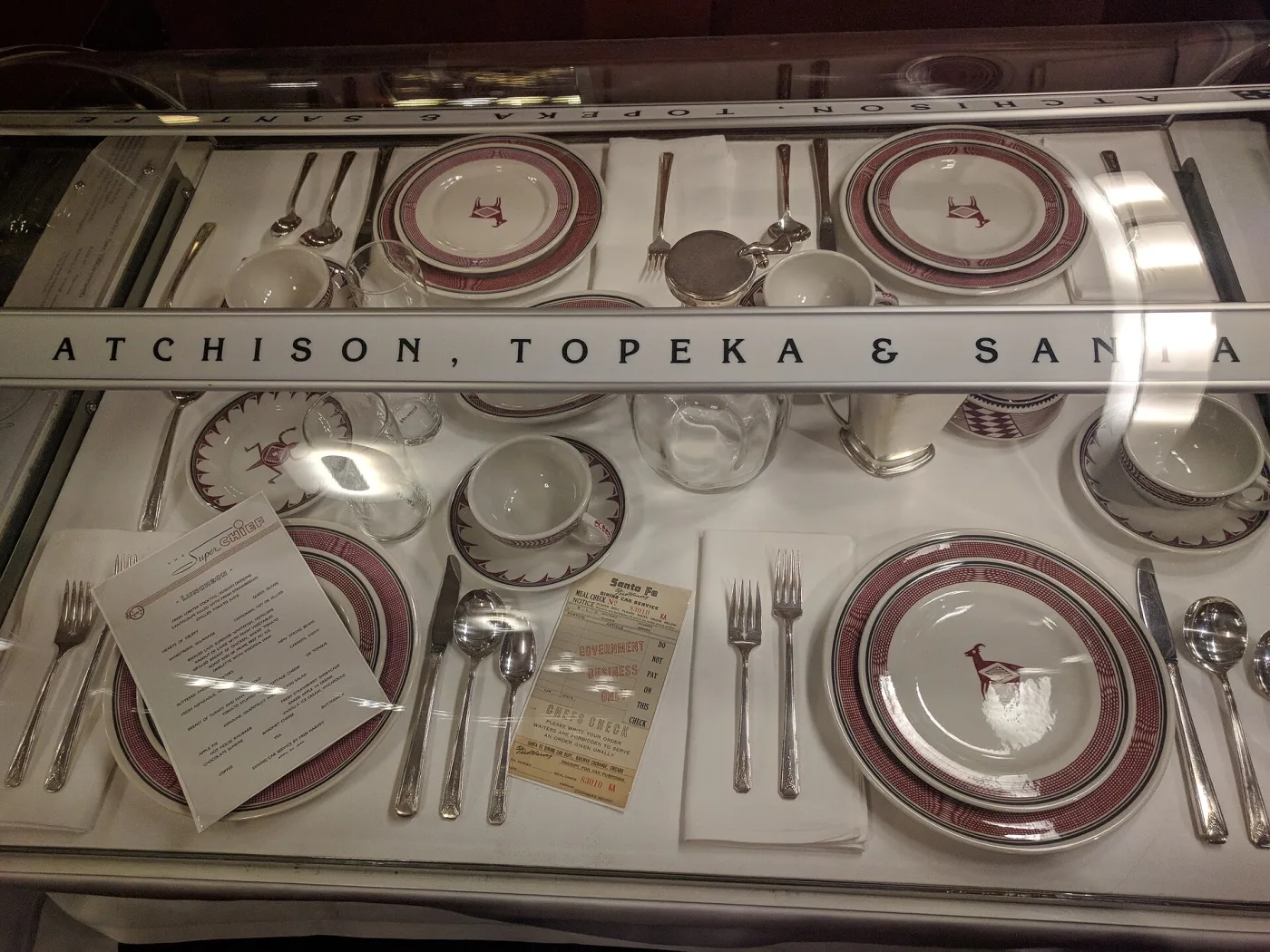 Museum case of Atchison, Topeka and Santa Fe dining car china, red and black Mimbres-style borders and animal figures, with a Super Chief luncheon menu and a Fred Harvey meal check