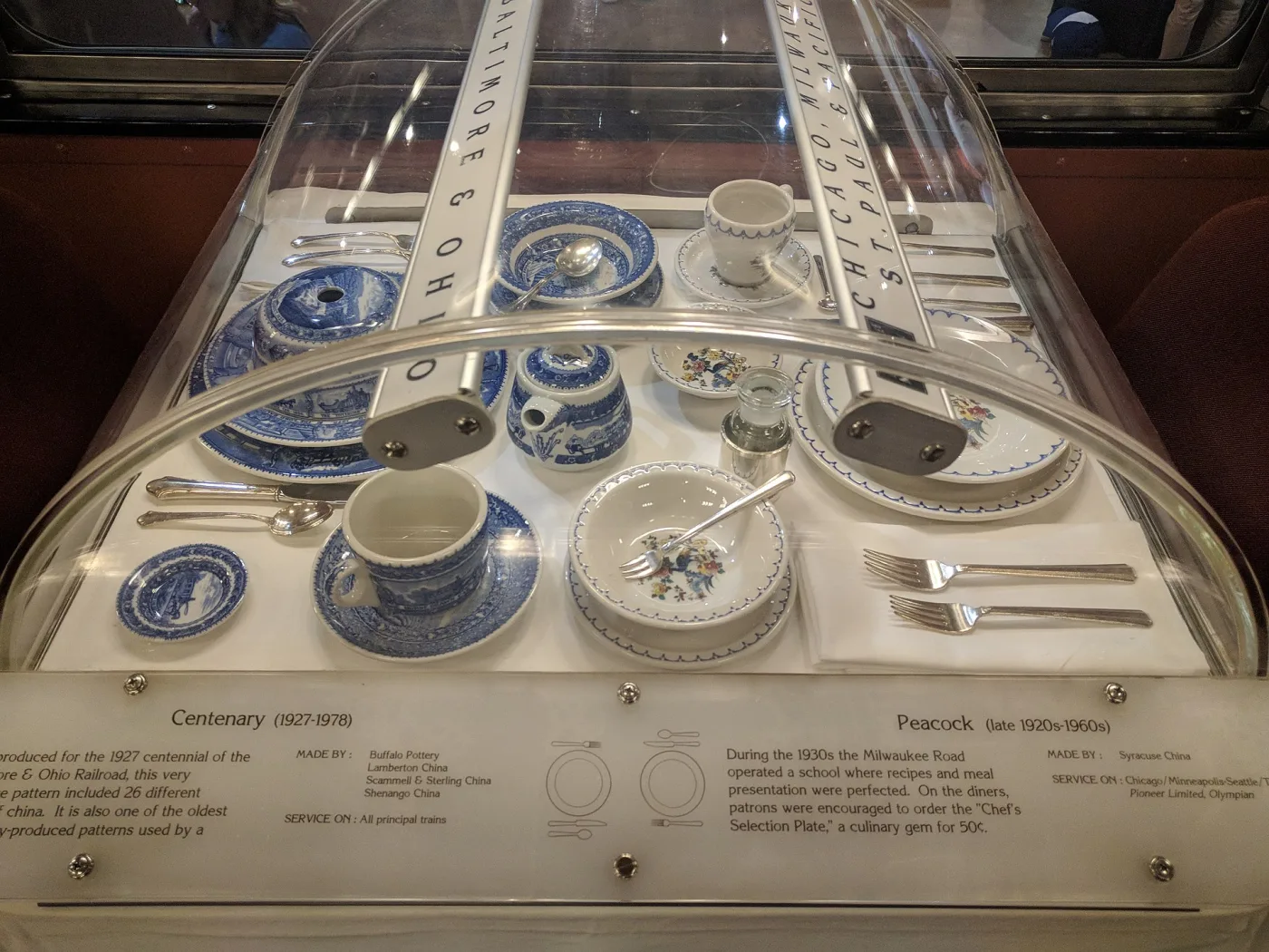 Museum case of blue transferware dining car china from the Baltimore and Ohio Railroad beside a floral pattern from the Milwaukee Road, with an interpretive label