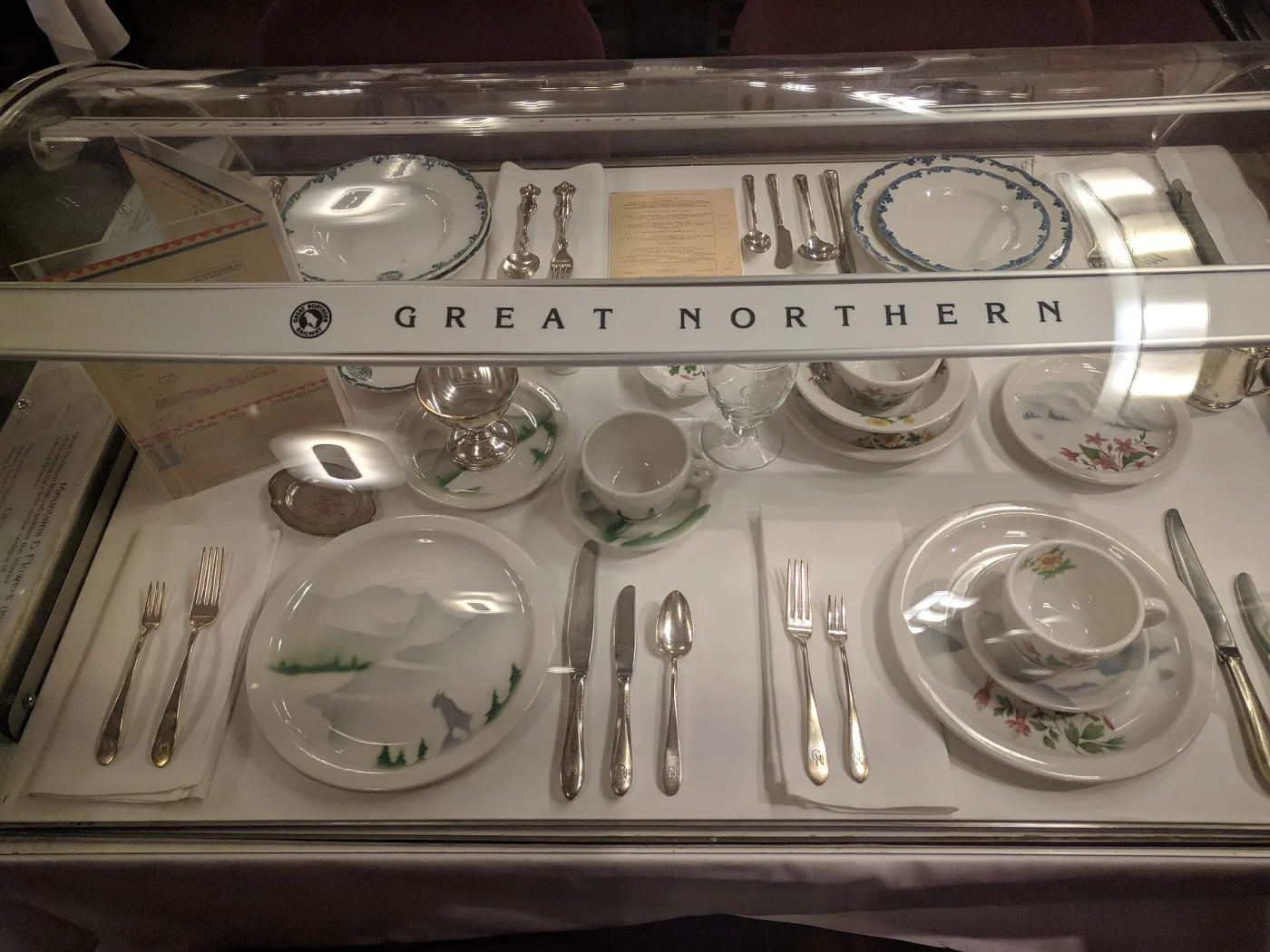 Museum case of Great Northern Railway china, one pattern showing an airbrushed mountain landscape with a goat and another scattered with pink and yellow flowers