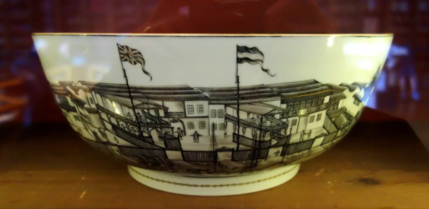 Chinese export punch bowl of about 1780 to 1785 painted in black and gold with a row of European trading factories along the Pearl River at Canton, national flags flying above them