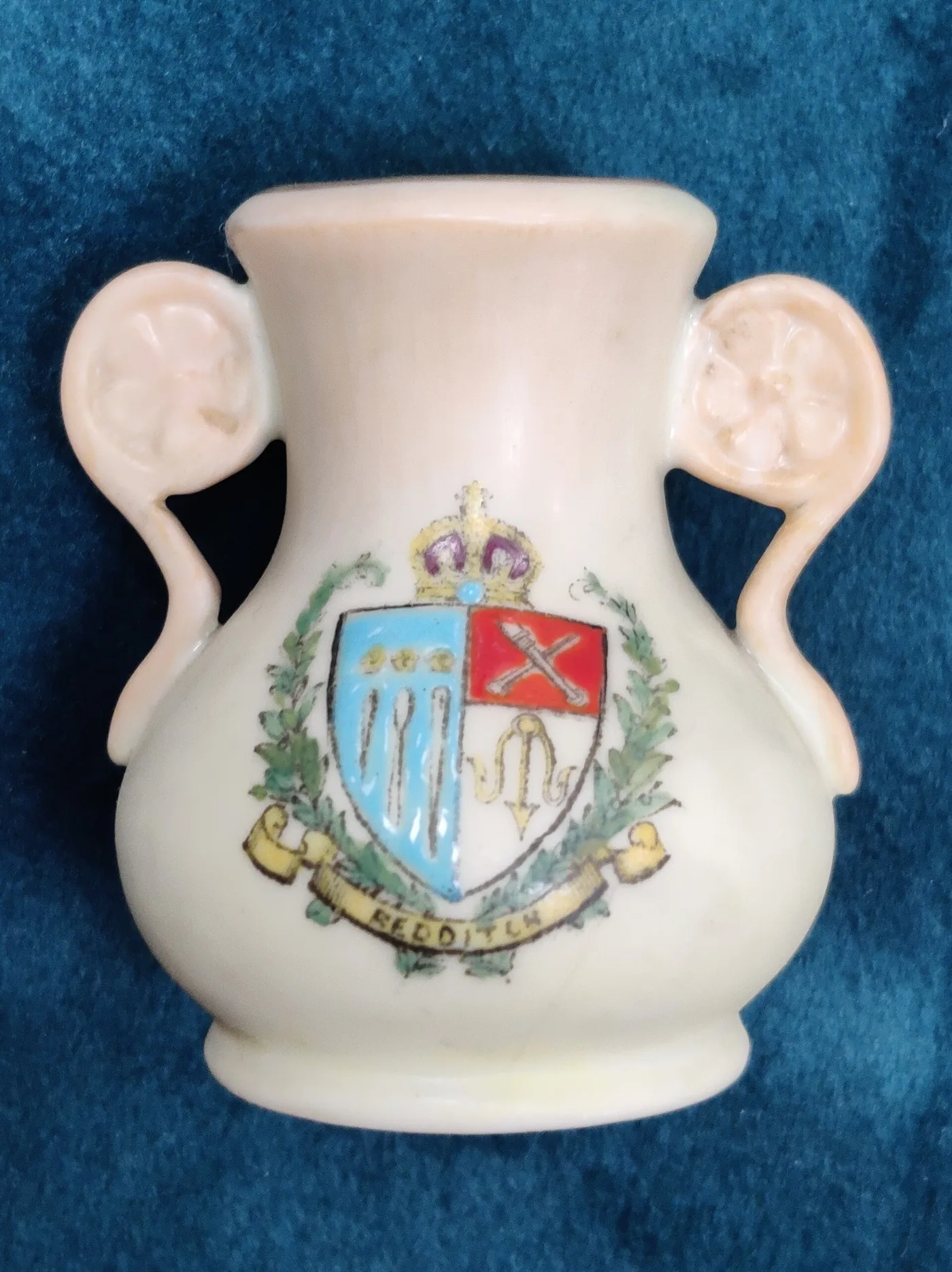 Small two-handled ivory-coloured vase printed with a crowned coat of arms and the name Redditch, photographed on blue cloth